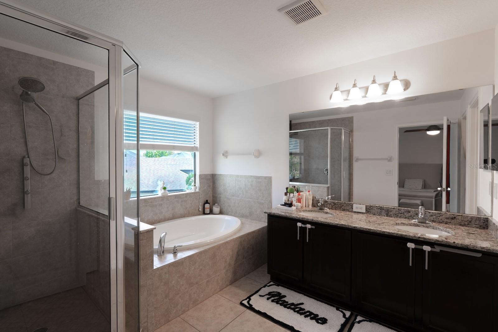 Spacious primary bathroom featuring dual vanity sinks, a glass-enclosed walk-in shower, and a relaxing garden tub.
