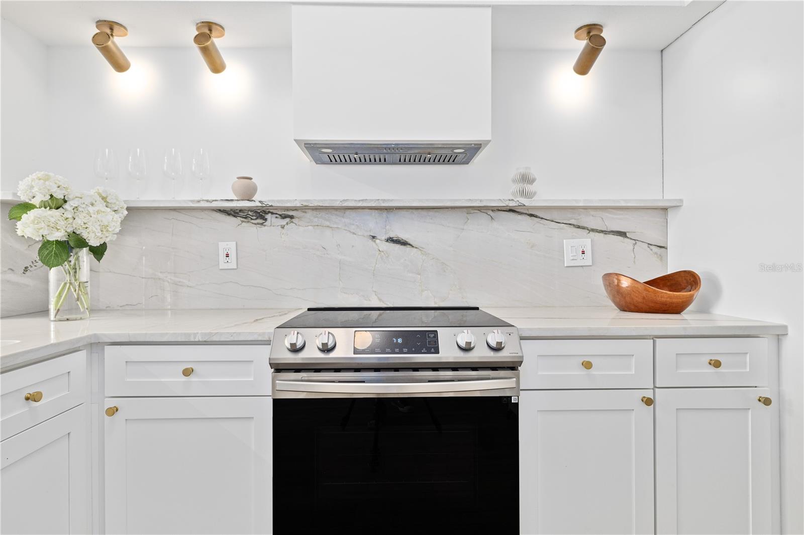 Open kitchen features an integrated hood and marble countertops that wrap the backsplash