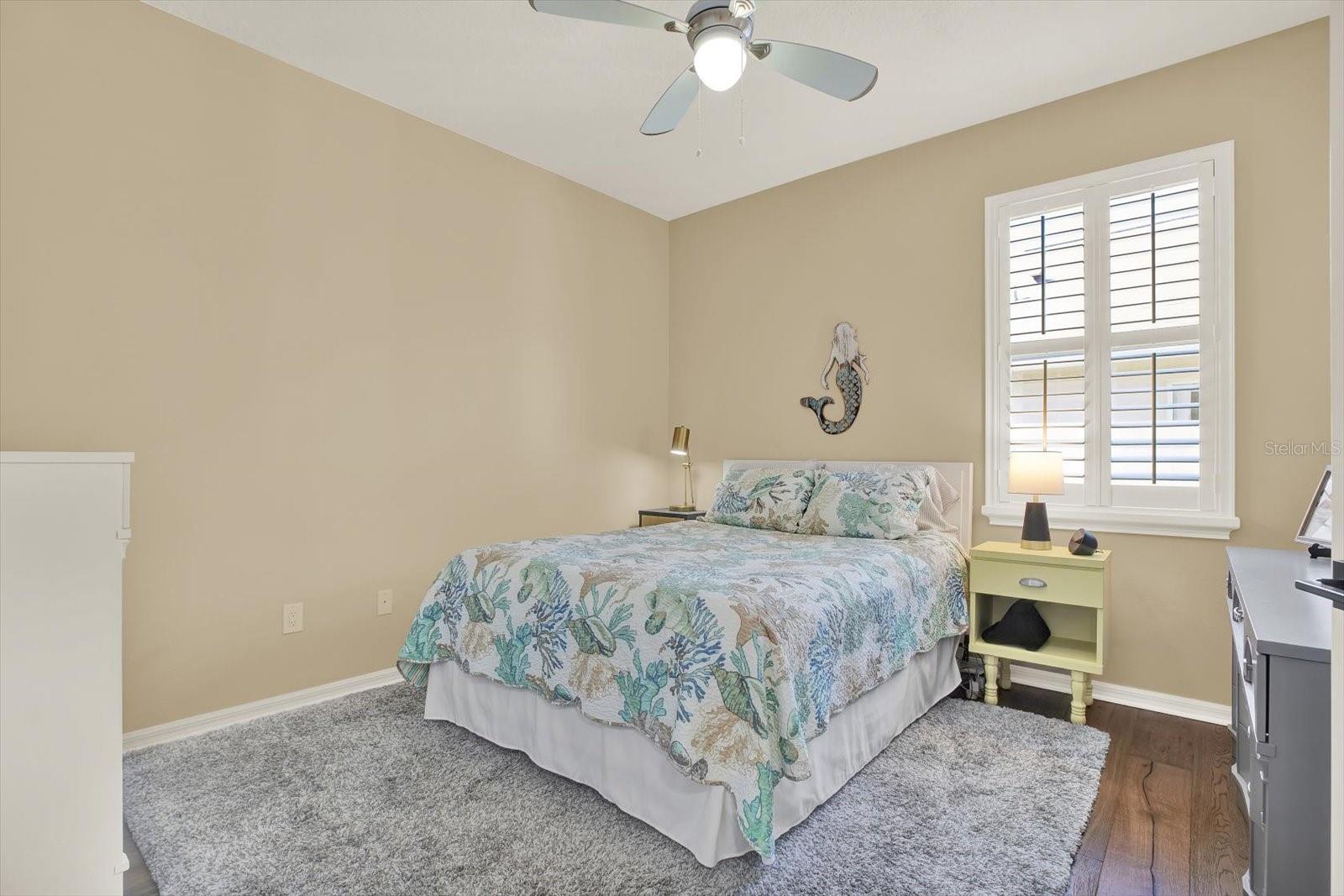 Cozy guest bedroom with oak hardwood floors, plantation shutters, and plenty of natural light—perfect for visitors or a peaceful retreat.
