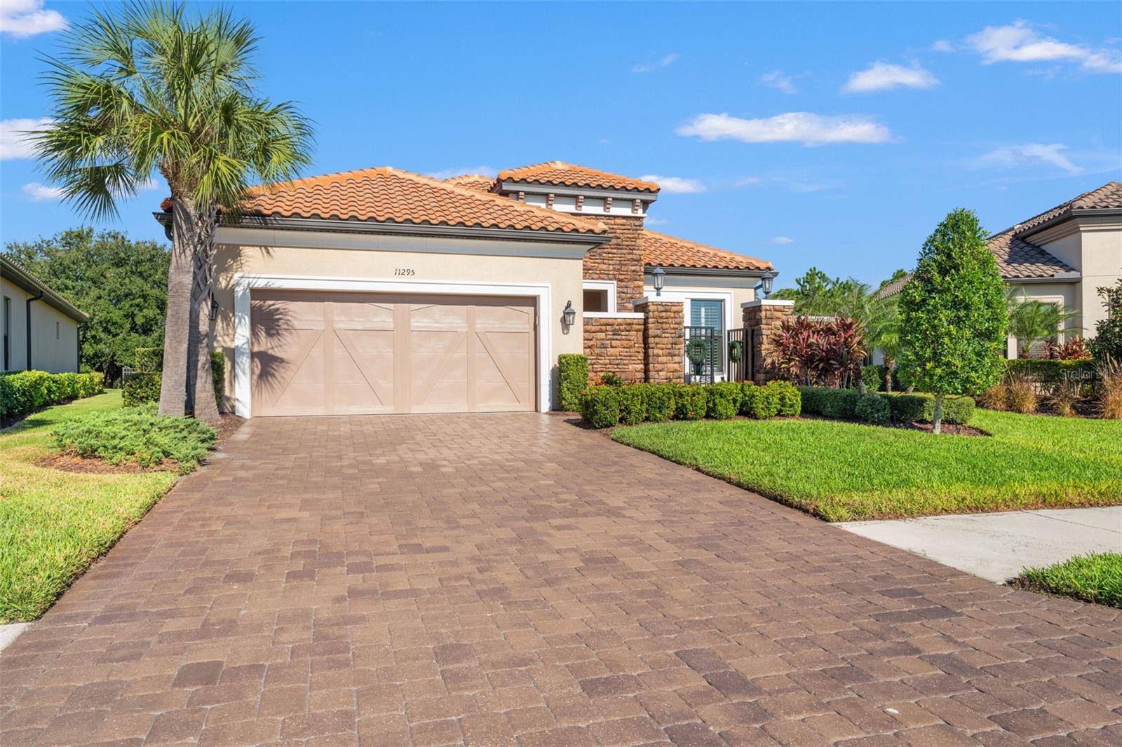 Striking Mediterranean-style exterior with tile roof, stone accents, and paver driveway beautifully illuminated at dusk.