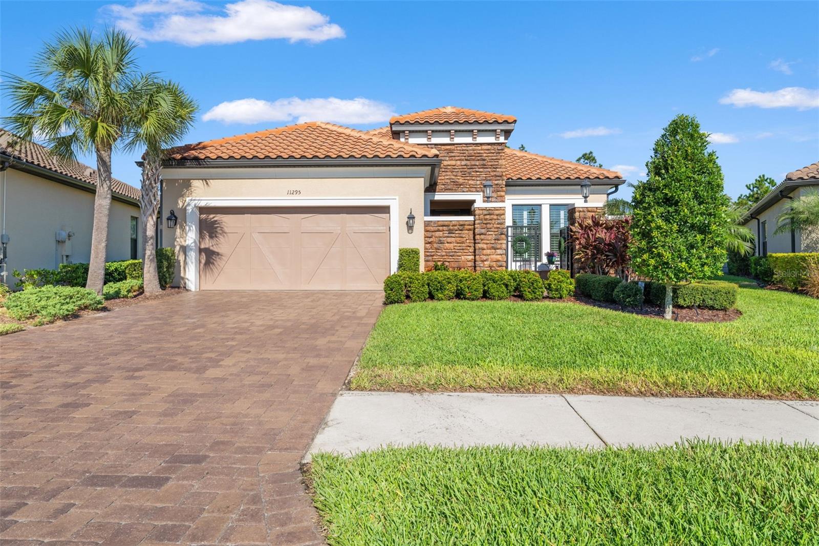 Front elevation with lush landscaping, manicured hedges, and a gated courtyard entry providing privacy and curb appeal.