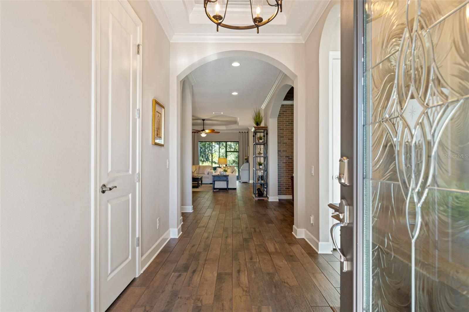 Welcoming foyer with porcelain tile flooring, crown molding, and arched entries leading to open living spaces.