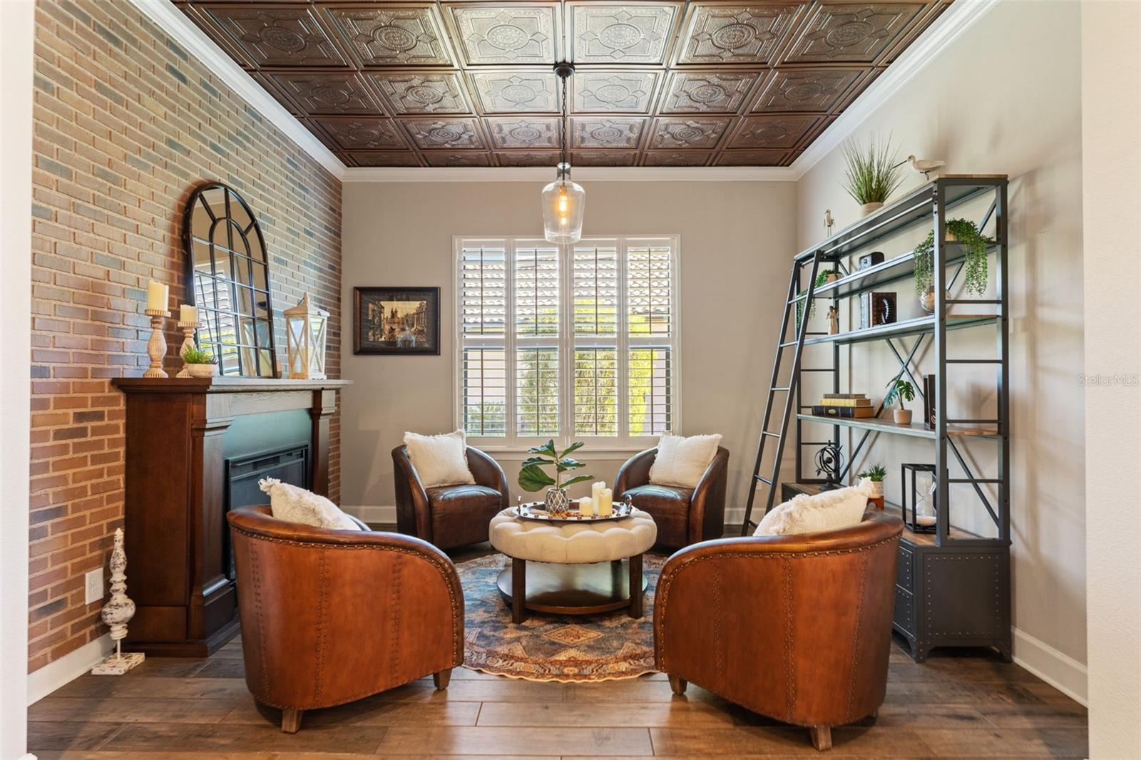Library or den with brick accent wall, decorative fireplace, and coffered ceiling—perfect for quiet reading or conversation.