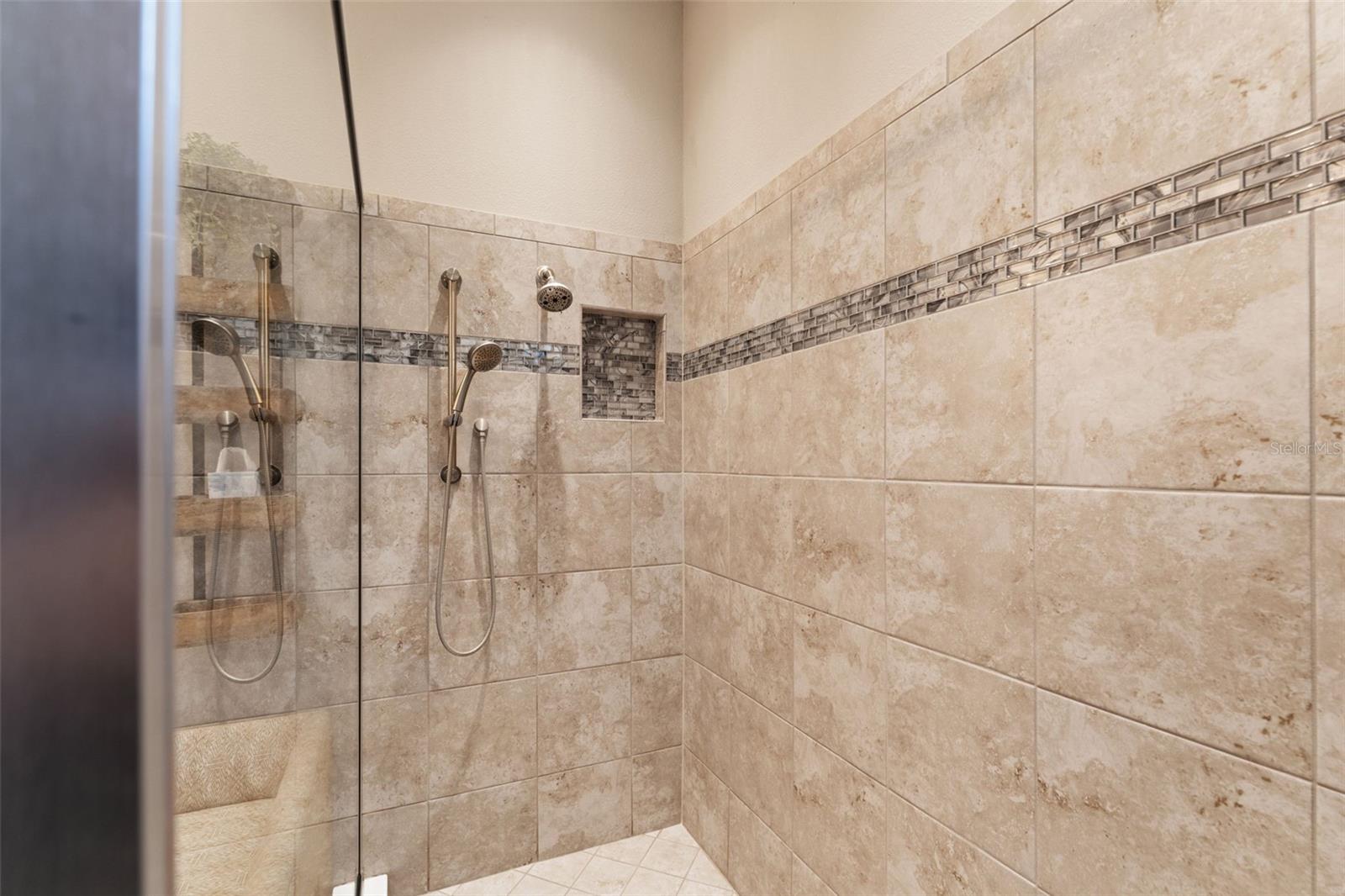 Beautifully tiled walk-in shower with decorative glass inlay and dual shower heads, combining spa-level luxury with everyday practicality.