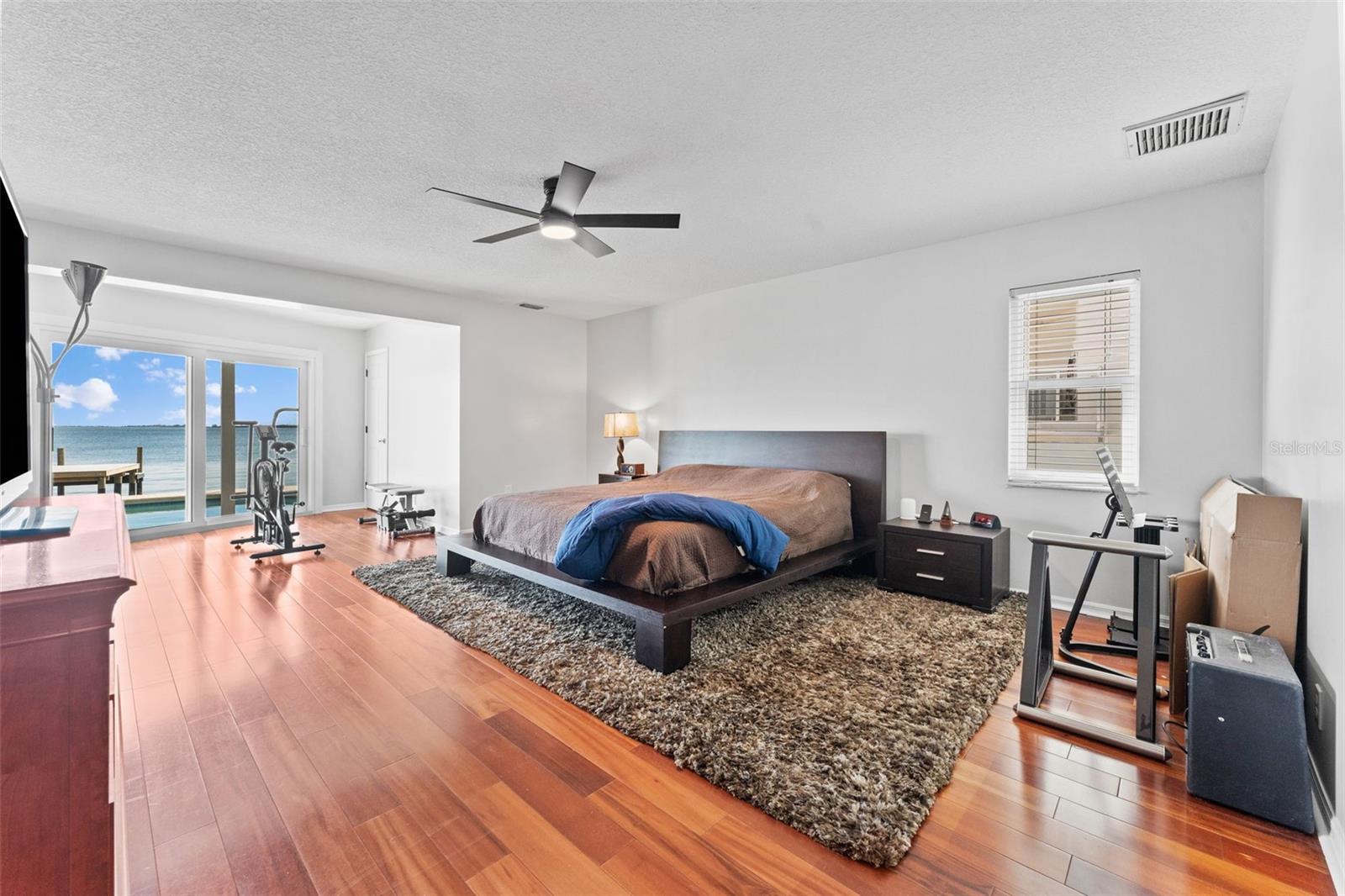 Expansive primary bedroom with sliding glass doors that open to the pool deck and showcase stunning waterfront views.