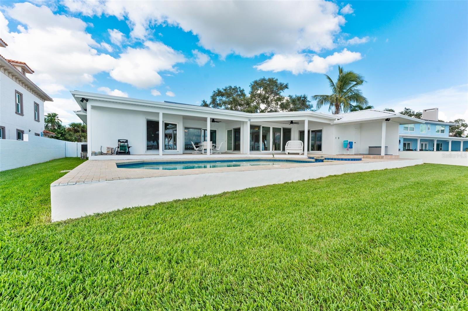 Beautiful outdoor space viewed from the seawall, showcasing the pool, patio, and backyard leading up to the home.