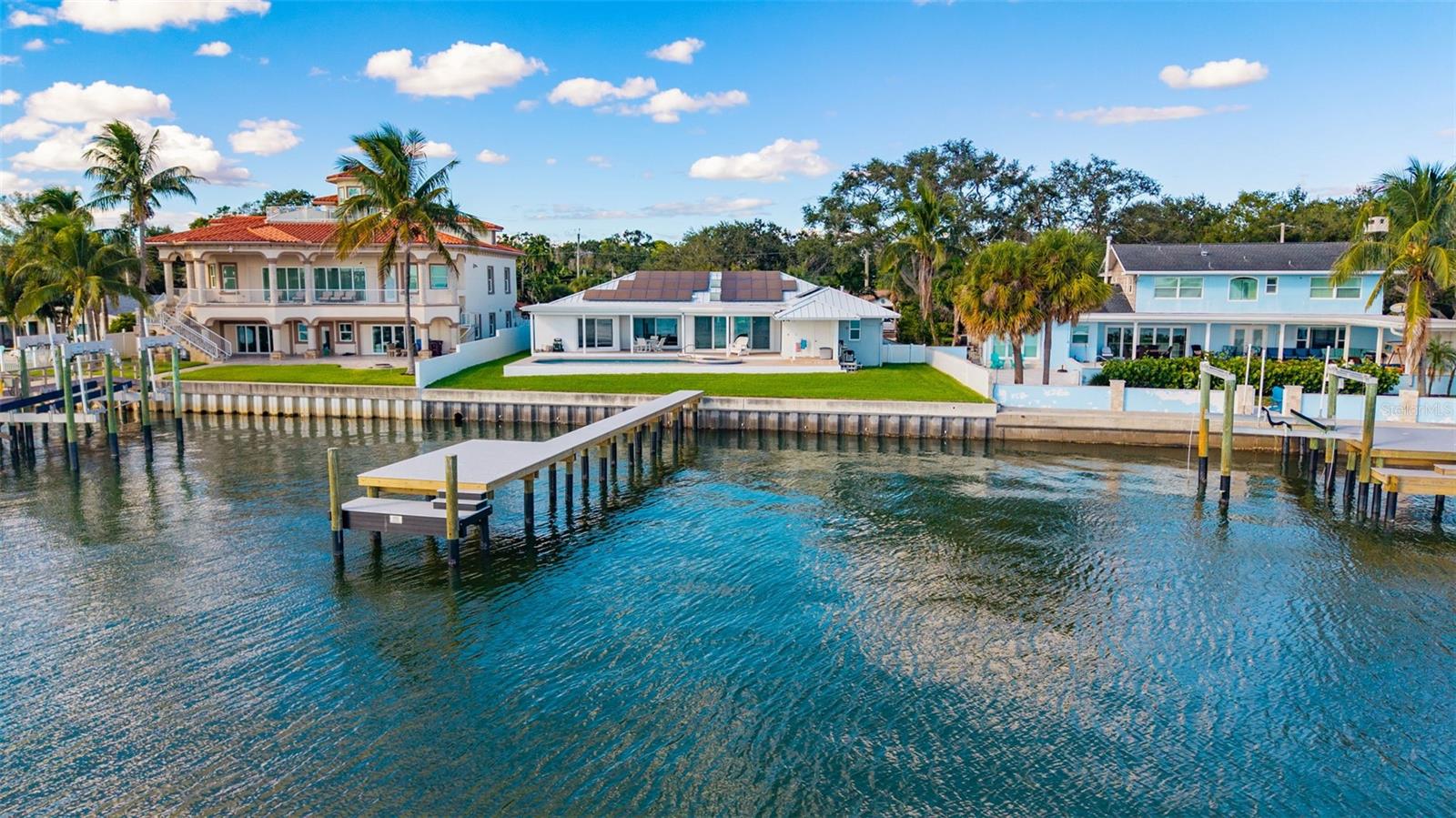 Drone view from the water highlighting the backyard, pool, home, and newly installed dock, all set against stunning waterfront scenery.