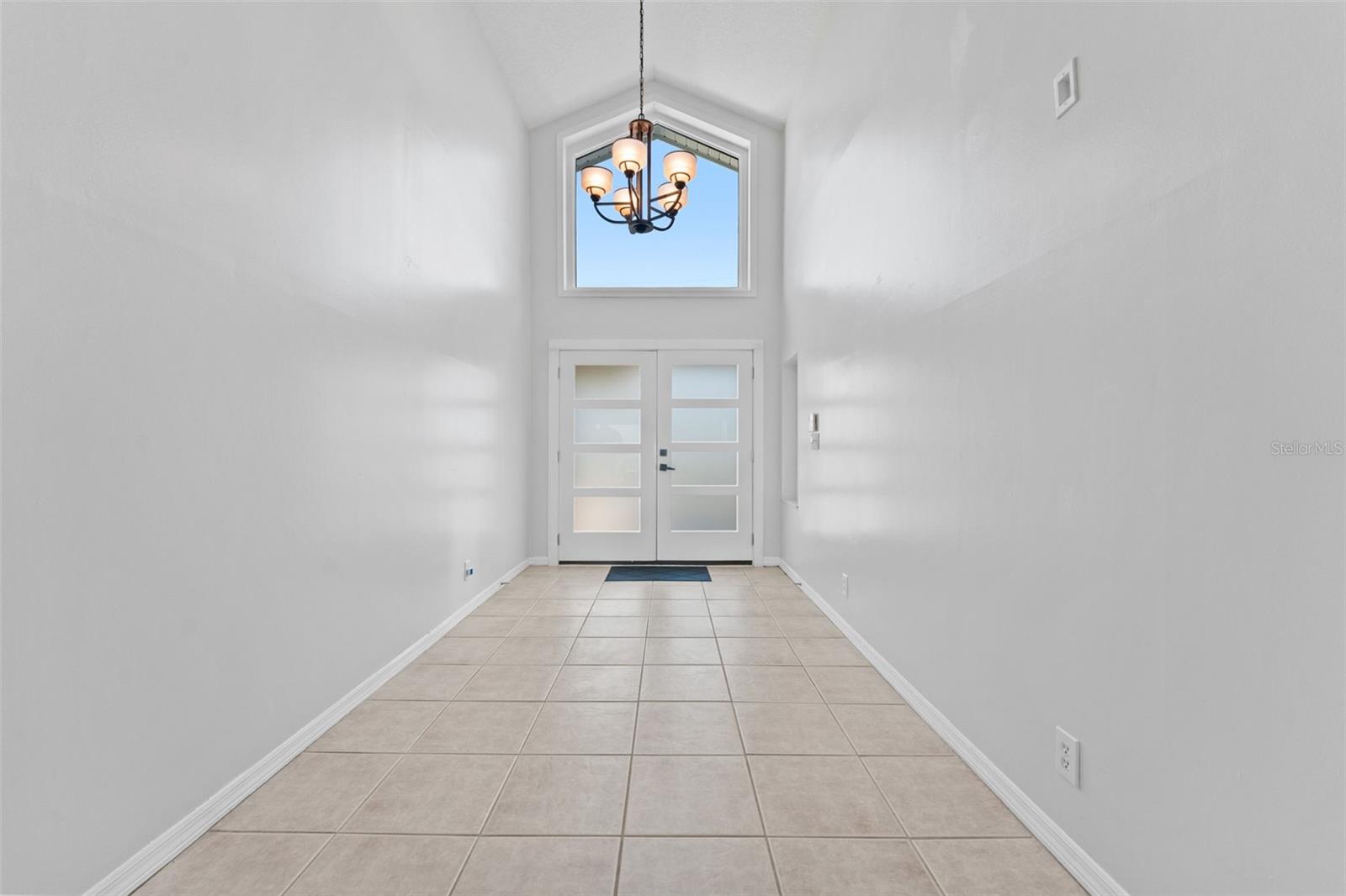 Bright and welcoming entryway featuring a large window above the double doors and a modern light fixture that enhances the natural light.