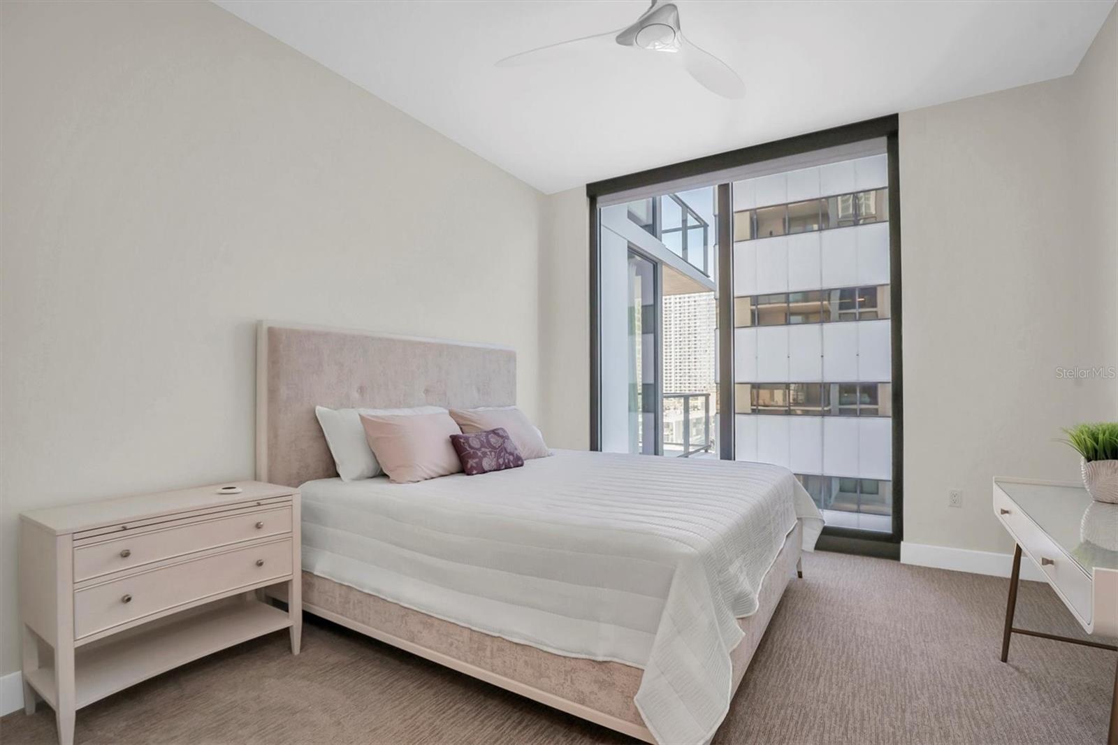 Bright second bedroom boasts a floor-to-ceiling window complemented by custom shades