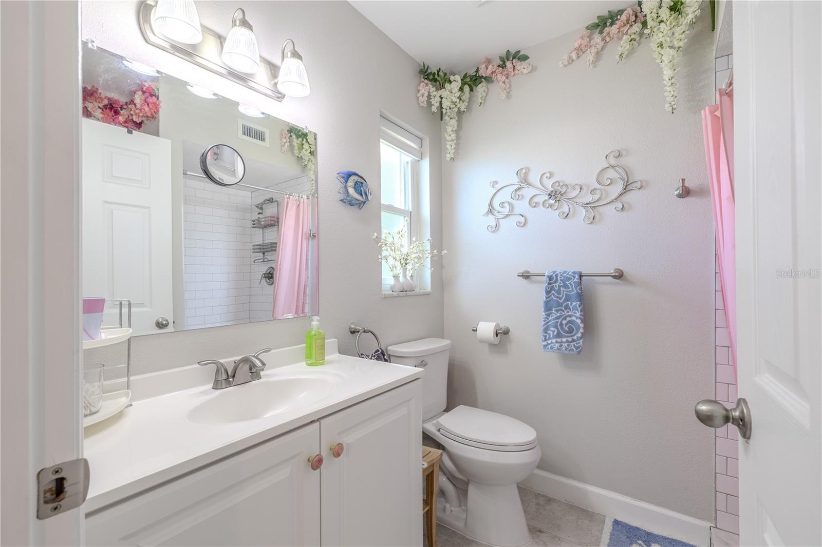 Updated primary bath with tiled walk-in shower, extended vanity, and bright lighting. A recessed storage nook behind the door provides smart, discreet organization.