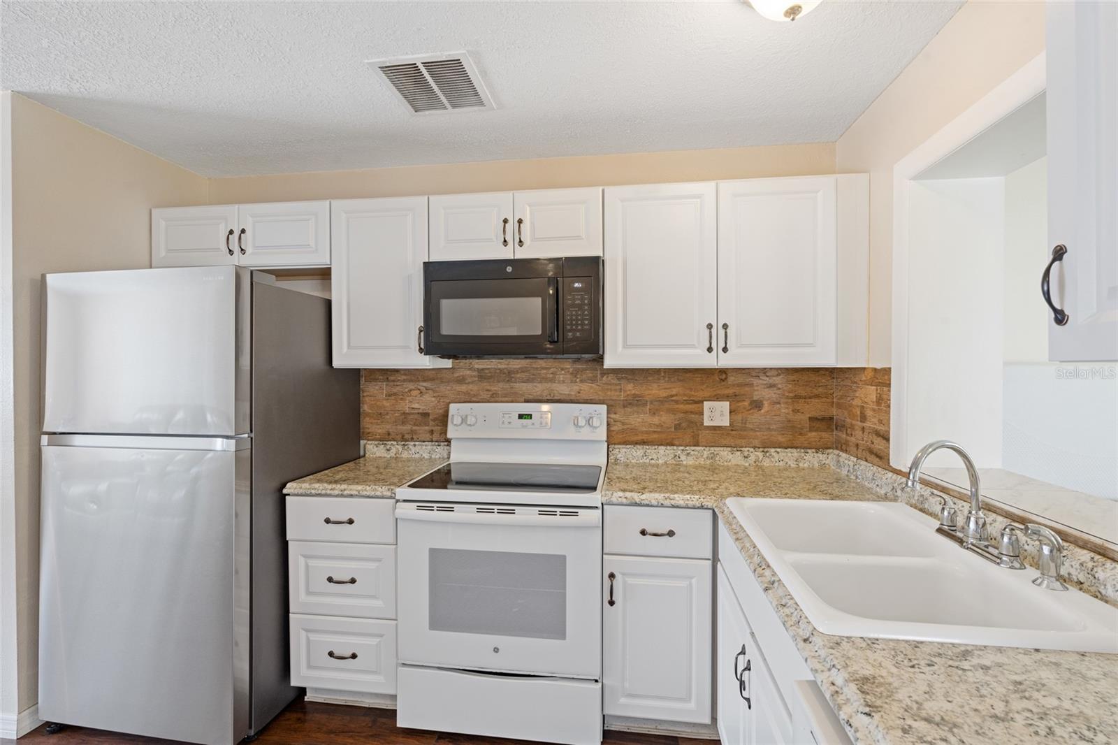 Updated kitchen with newer backsplash, counters and fridge.