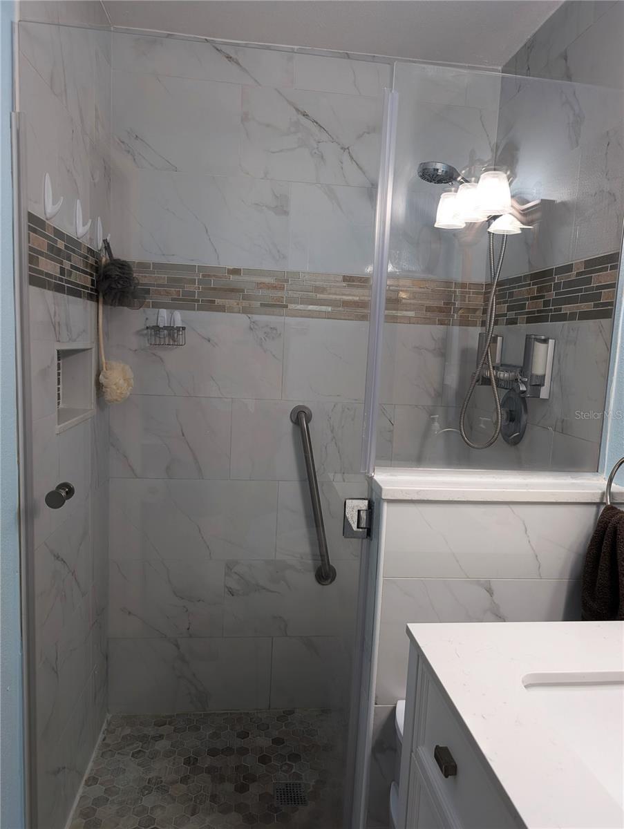 Stunning walk-in shower with glass shower door, satin nickel hardware, glass tile accent and safety grab bars.