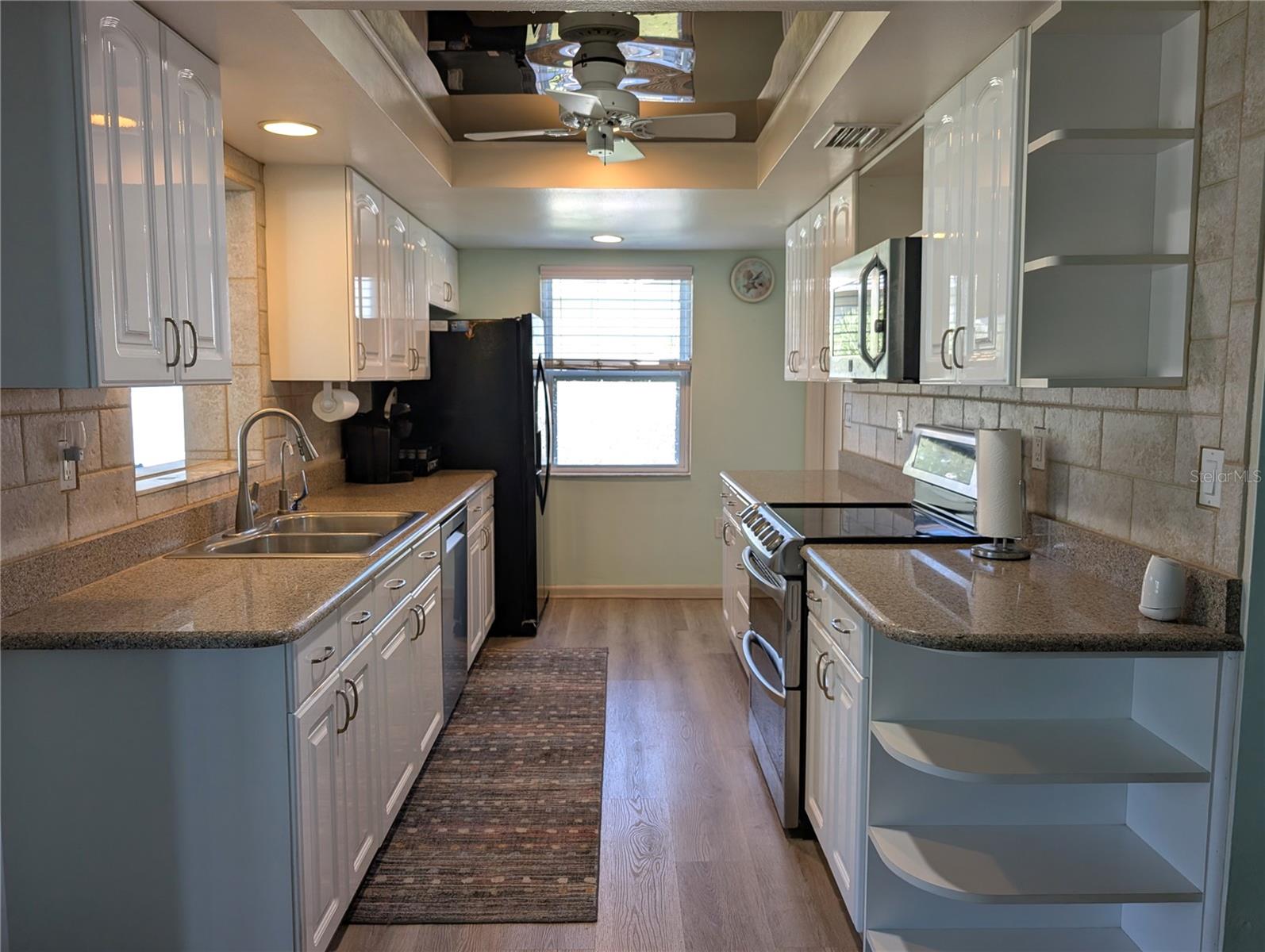 Updated galley kitchen features vinyl flooring, granite countertops, white cabinetry, custom tray ceiling, inset lighting and brushed nickel assessories.
