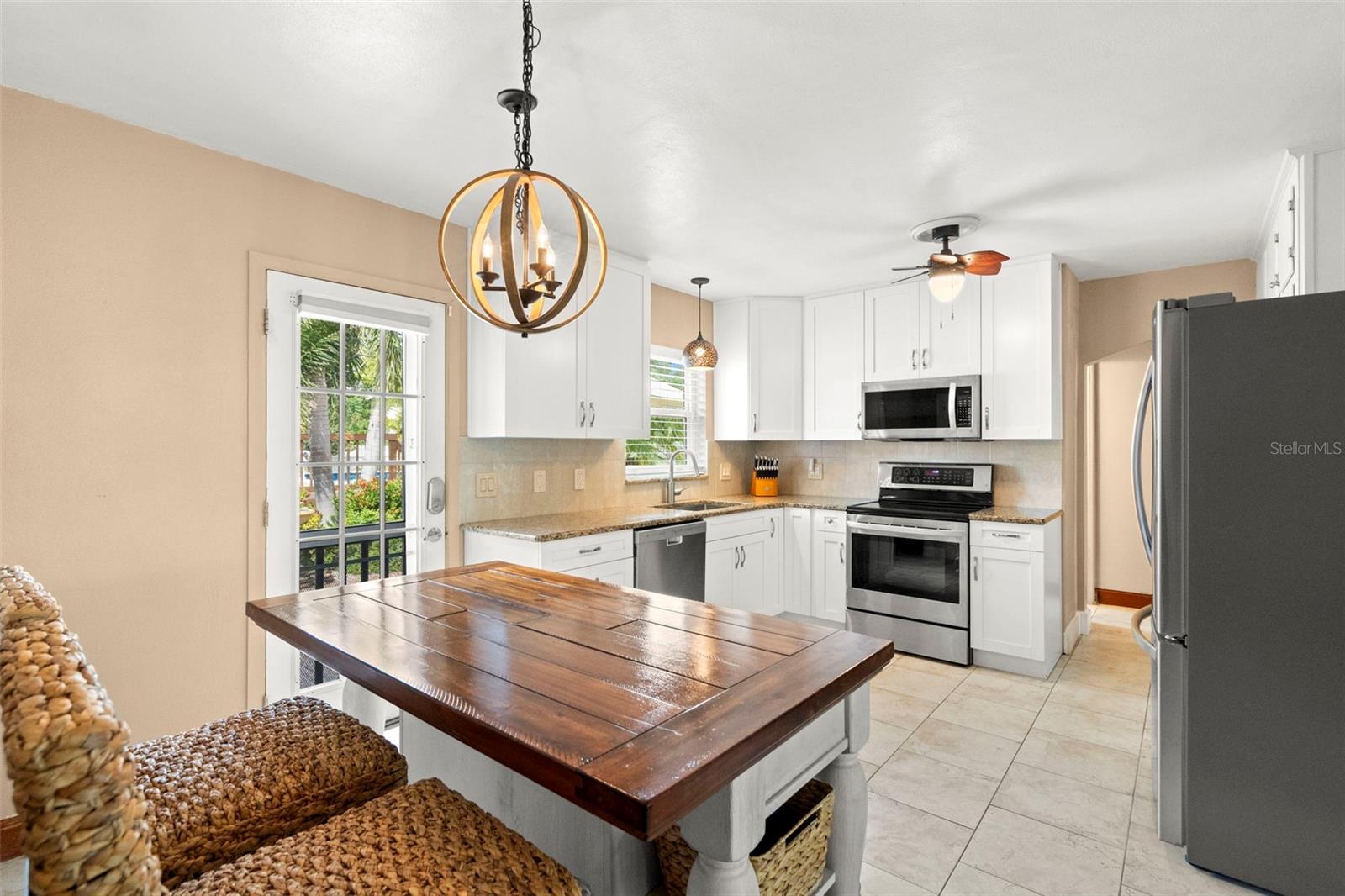 The kitchen features extended white shaker cabinetry, stone countertops, a standalone pantry, glass front display storage, stainless steel appliances, and stylish lighting.