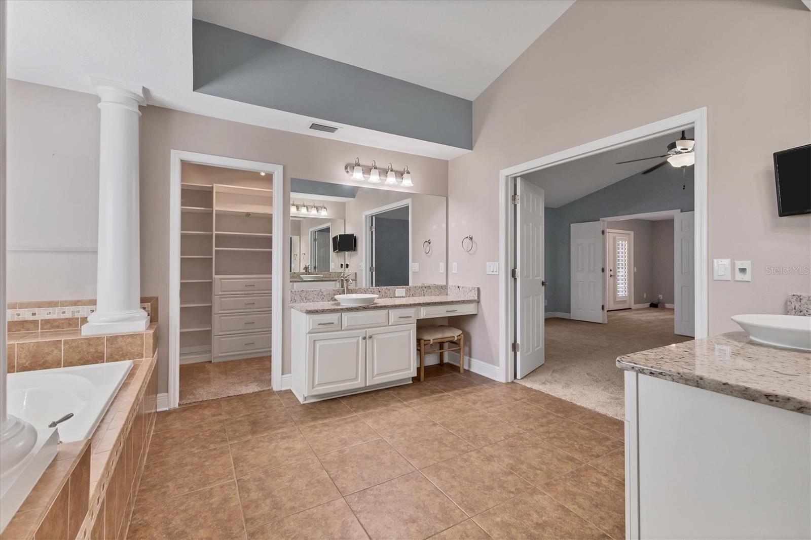 Large walk-in closet spans the length of bathroom and features custom shelving and drawers.  Vanity includes beauty bar with drawer and stool