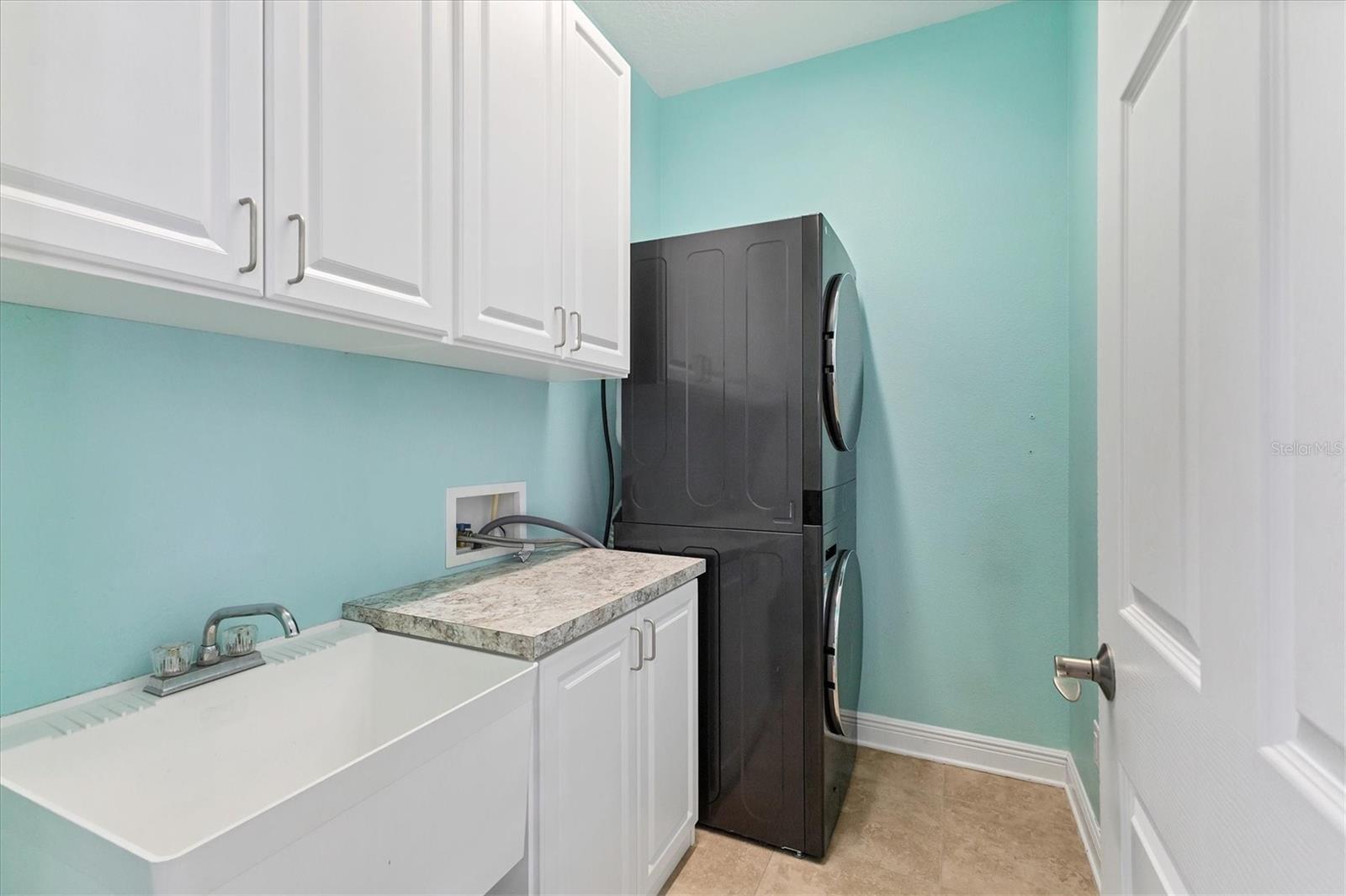 Laundry room offers a utility sink, storage cabinets, a counter for folding clothes and a full size front load washer and dryer set.
