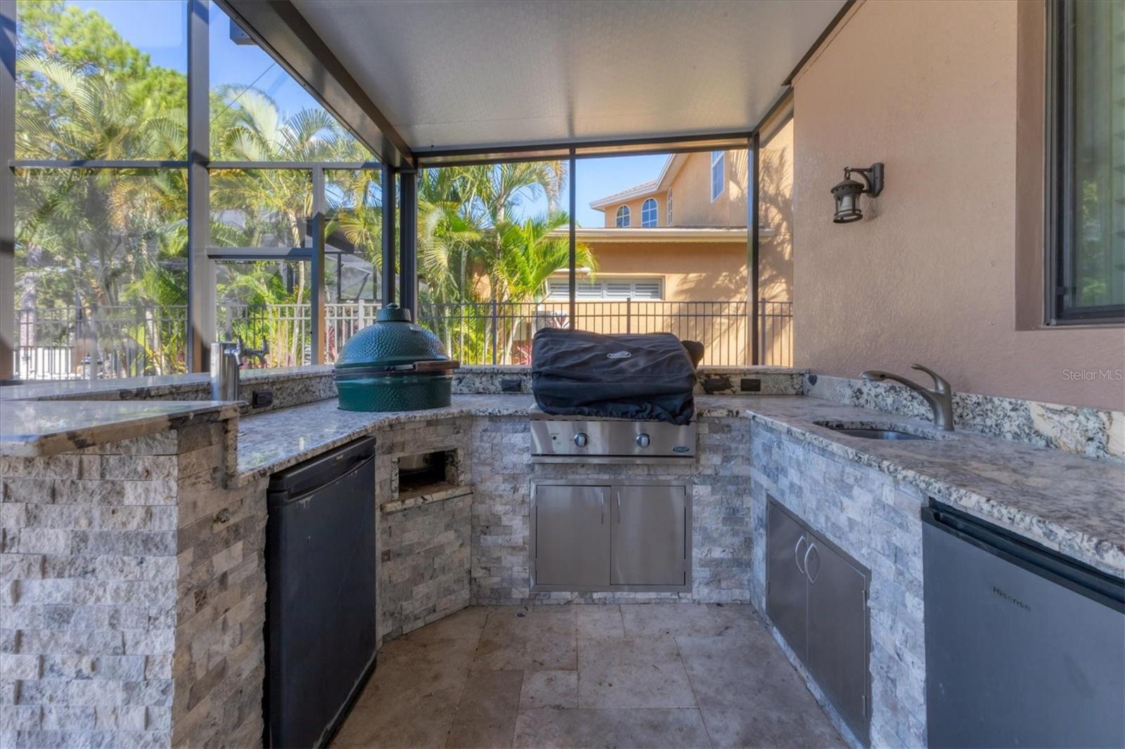 This outdoor kitchen boasts beautiful stonework & granite counters and bar top plus has a built-in grill, big Green Egg, sink and mini fridge making outdoor entertaining a breeze!