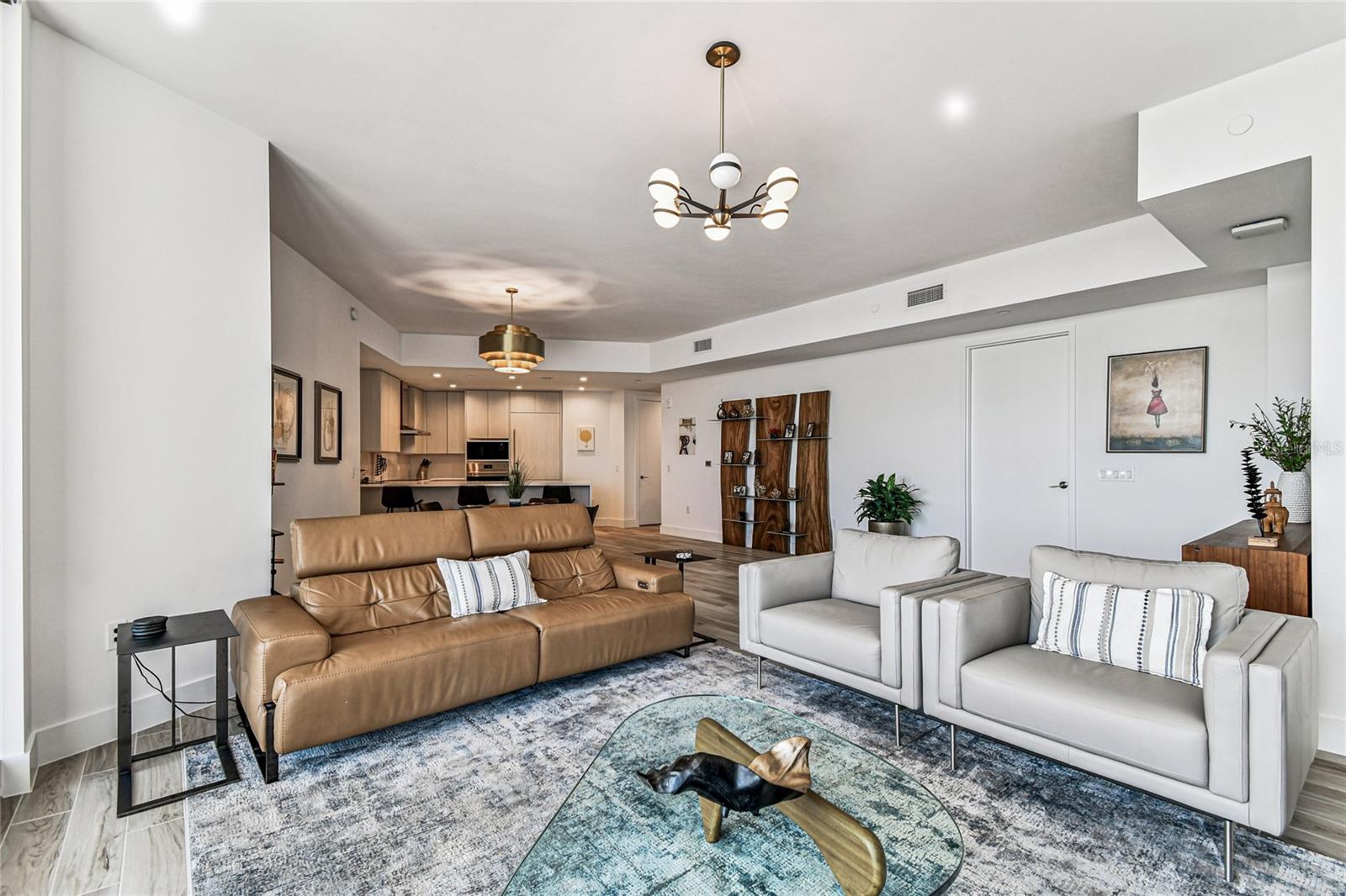 Spacious open-concept layout connecting living, dining, and kitchen, highlighted by modern lighting, neutral tones, and versatile furniture placement.
