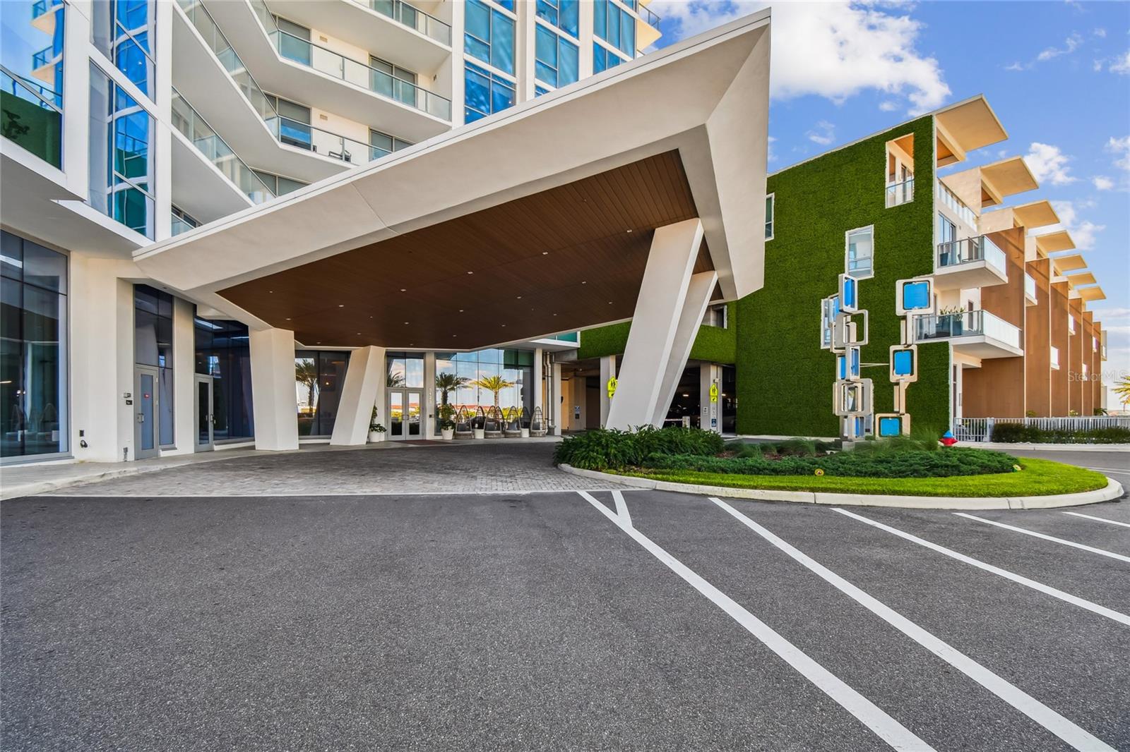 Dramatic porte-cochère with angular columns and wood-accent canopy, set against a modern glass façade and landscaped roundabout for easy resident drop-off.