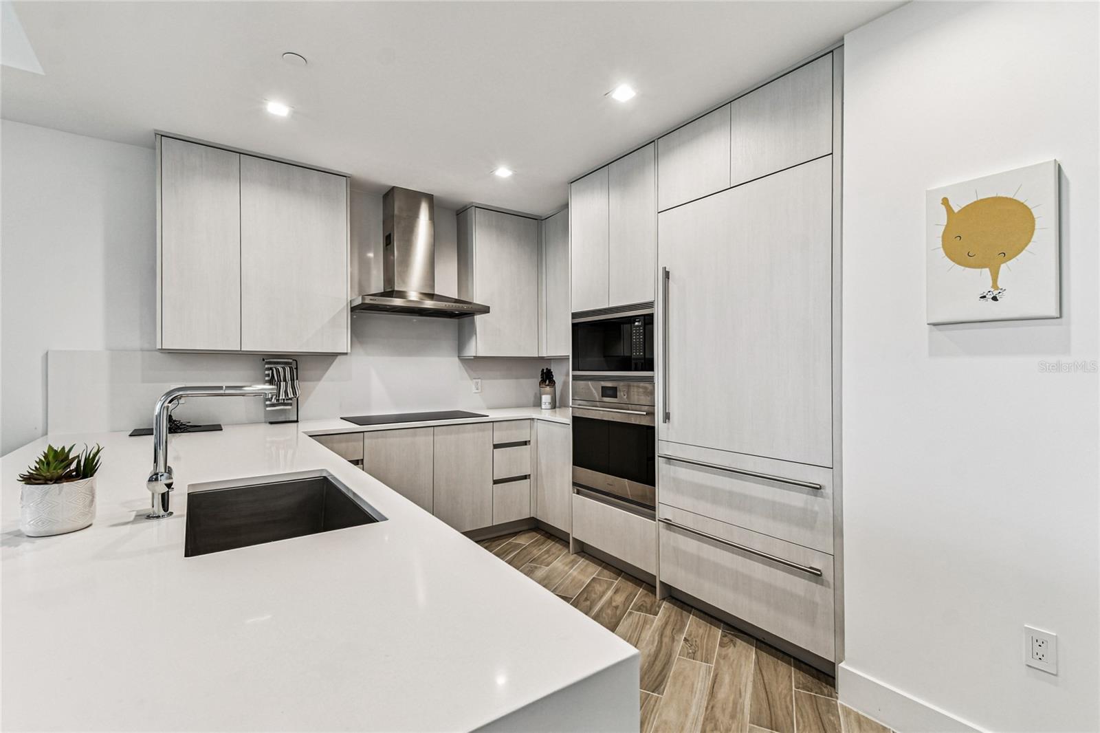 U-shaped prep layout with undermount sink, stainless hood, and abundant storage; wood-look tile carries through for a cohesive finish.