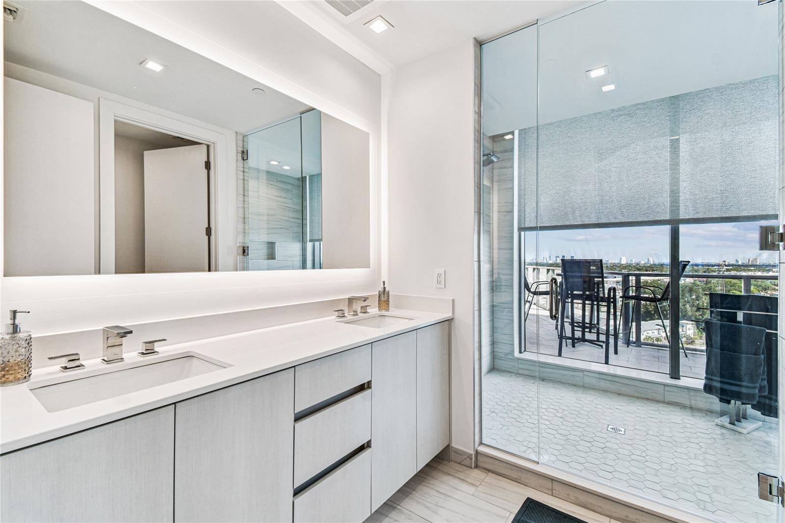 Primary Bathroom – Double vanity with backlit mirror and a frameless glass shower; clean lines and light finishes create a spa-like feel.