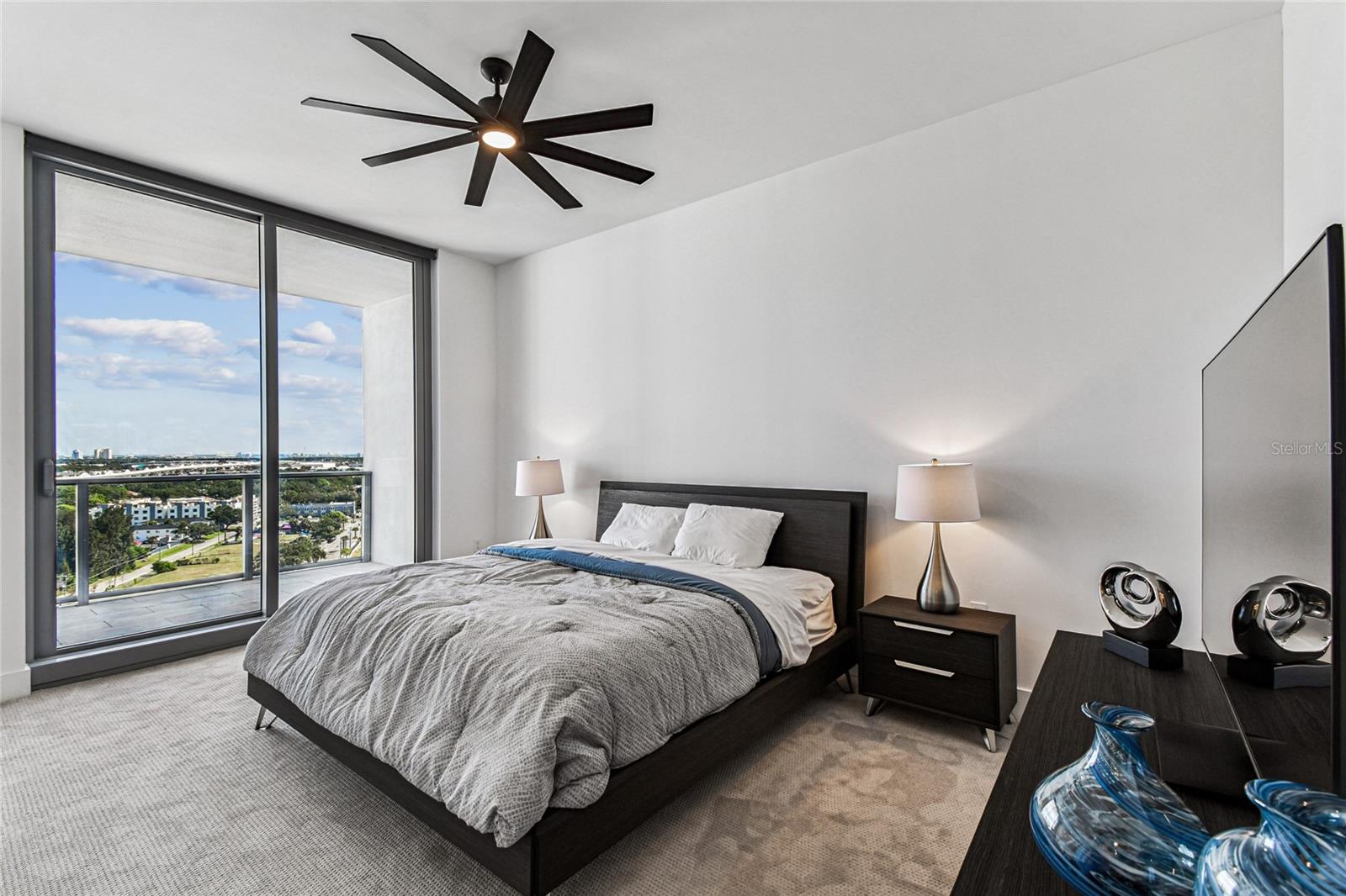 Primary Bedroom – Serene bedroom with expansive sliding glass doors to the balcony, a modern ceiling fan, and far-reaching city and water-view vistas.