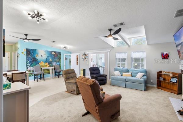 Enjoy the open floor plan of this spacious TV room with a fireplace, new ceiling fans, large screened-TV, and light fixtures.
