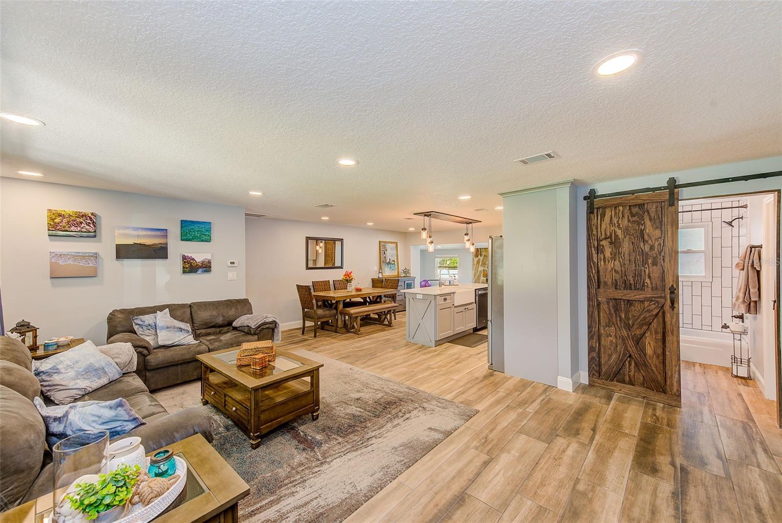 Open concept living room, looking into kitchen and dining.  Custom barn door to bathroom