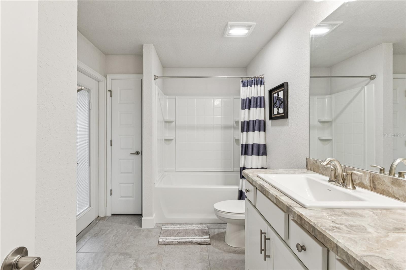 Guest bathroom with a tub, linen closet, and entrance to the back patio.