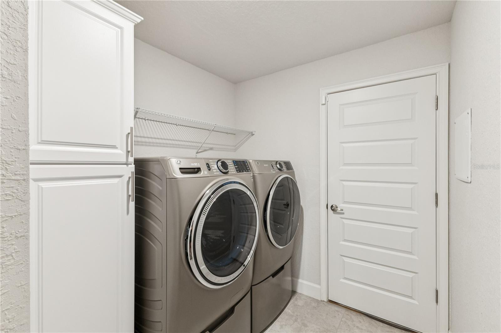 This laundry room can fit large appliances with a closet for storage and an entrance to the garage.