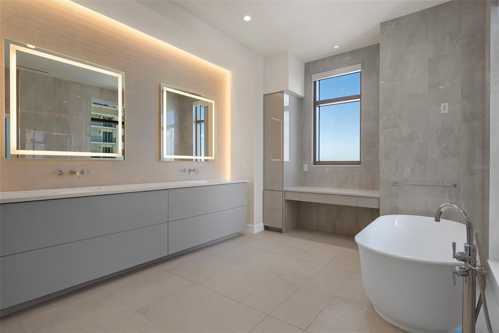 Dual vanities with backlit mirrors and makeup station. Designer tile and elegant finishes.