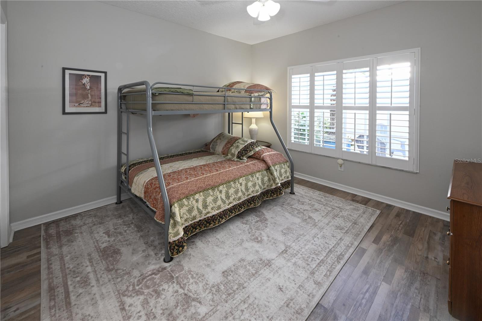 Guest Bedroom with vinyl flooring overlook front courtyard with a large window with shutters.