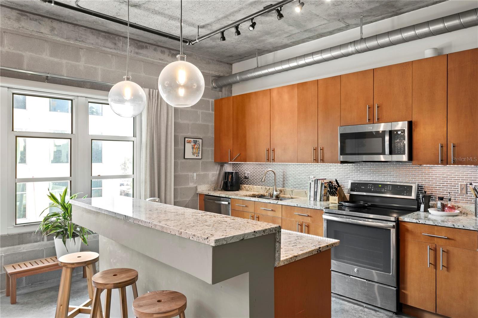 Modern kitchen with sleek cabinetry, granite countertops, pantry and stainless appliances and barstool seating for guests