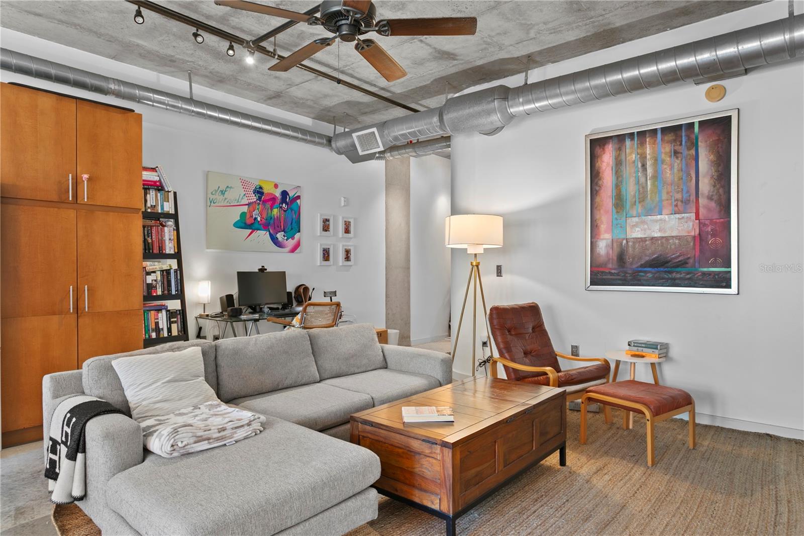 Stylish open-concept living space featuring modern industrial finishes, exposed concrete ceilings, and ductwork. Comfortable and bright with a versatile layout perfect for relaxing or working from home.