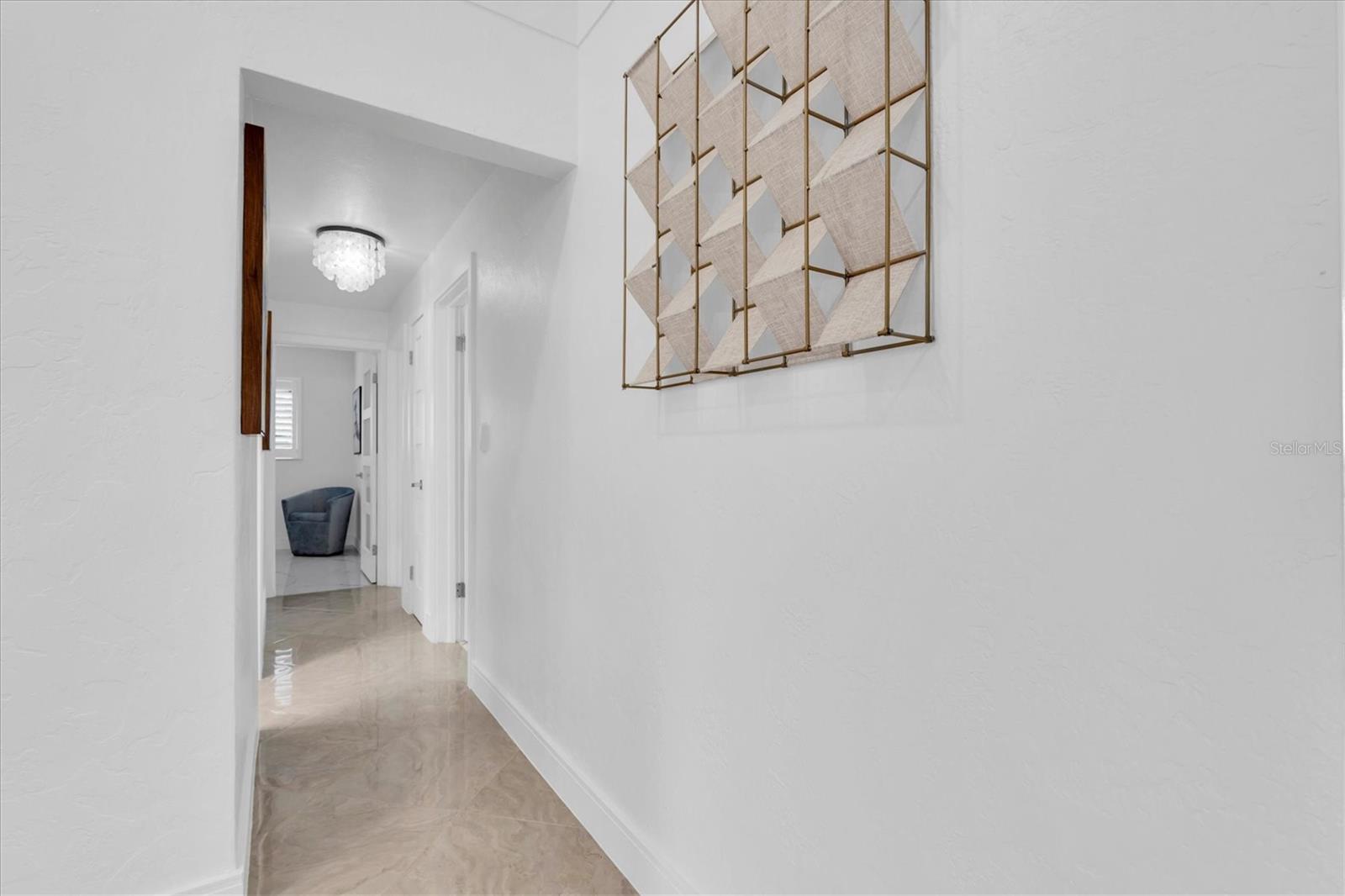 Designed with a split-bedroom floor plan, the primary suite is privately separated from the three additional bedrooms,  The light-filled hallway with porcelain floors connects to the three additional bedrooms.