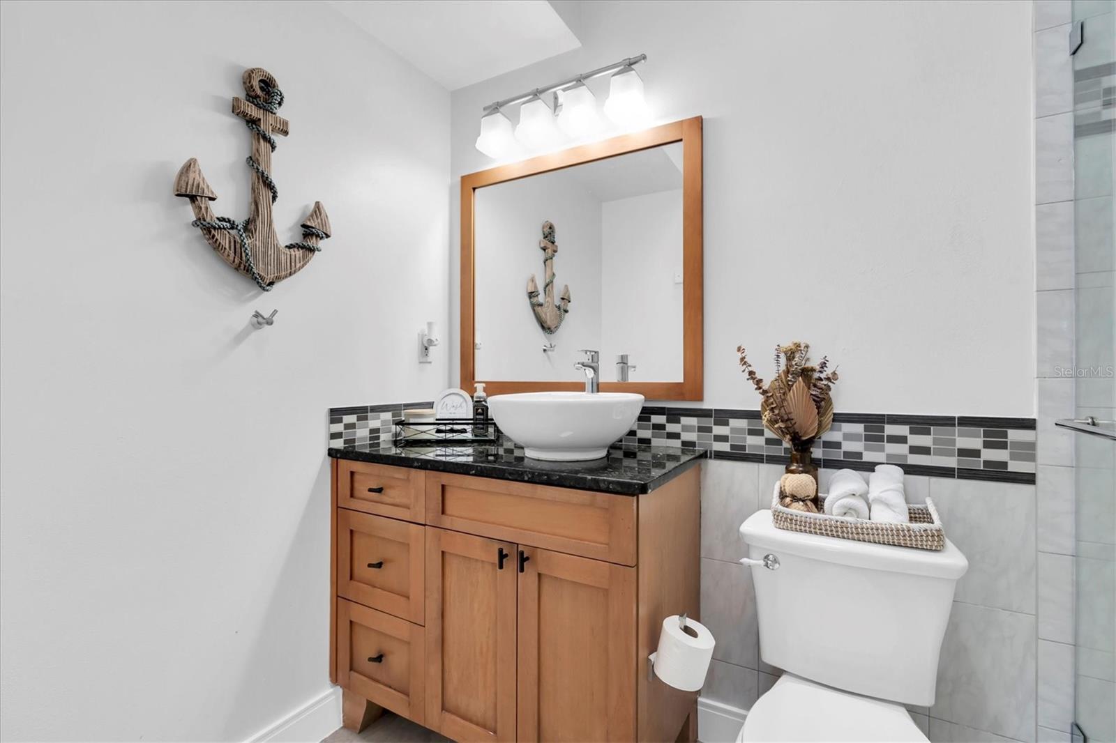 The second bathroom is beautifully appointed with wood cabinetry and a glass-enclosed shower with built-in niche.