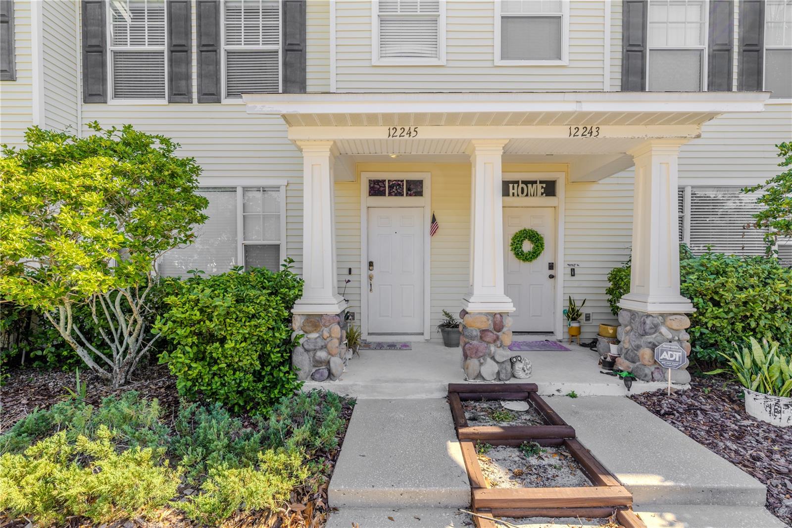 Surrounded by greenery, a trio of stone-tiered steps leads to a welcoming doorway flanked by columns that rise proudly from their stone foundations. The entrance feels both grounded and graceful—a perfect prelude to the warmth that lies within.