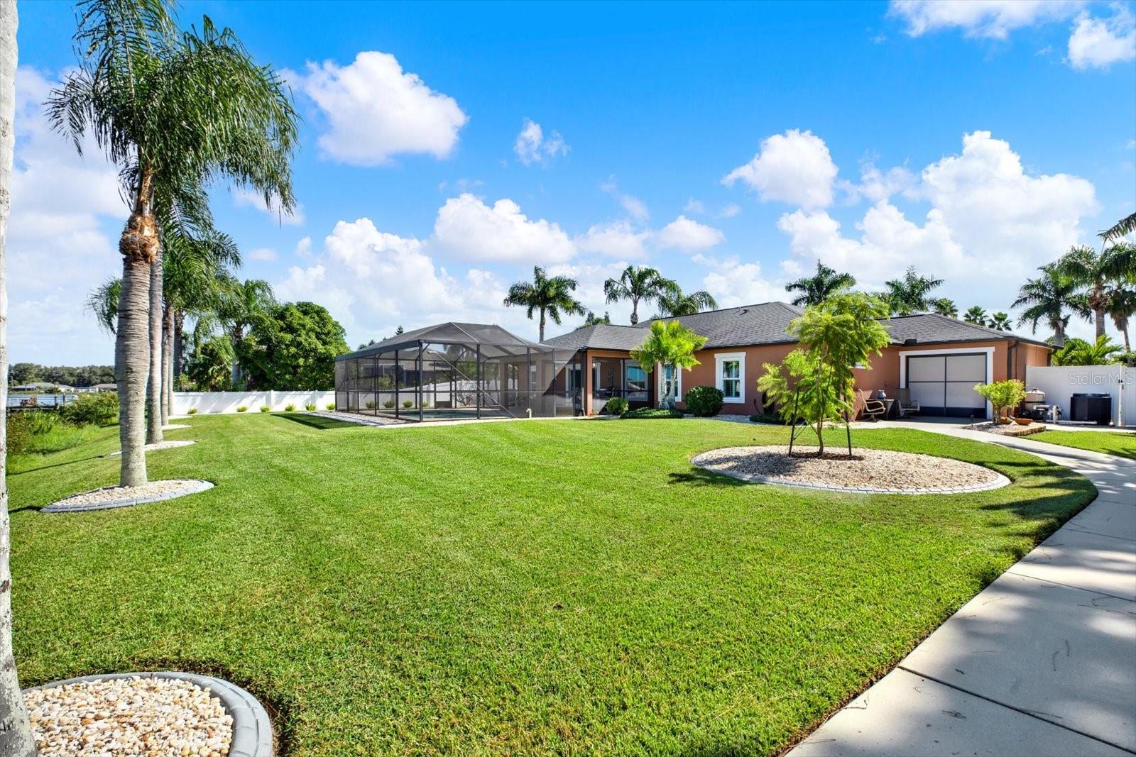 The meticulously landscaped oversized lakefront back has mature palms, borders, and a sidewalk from the drive-through garage door to the lake.