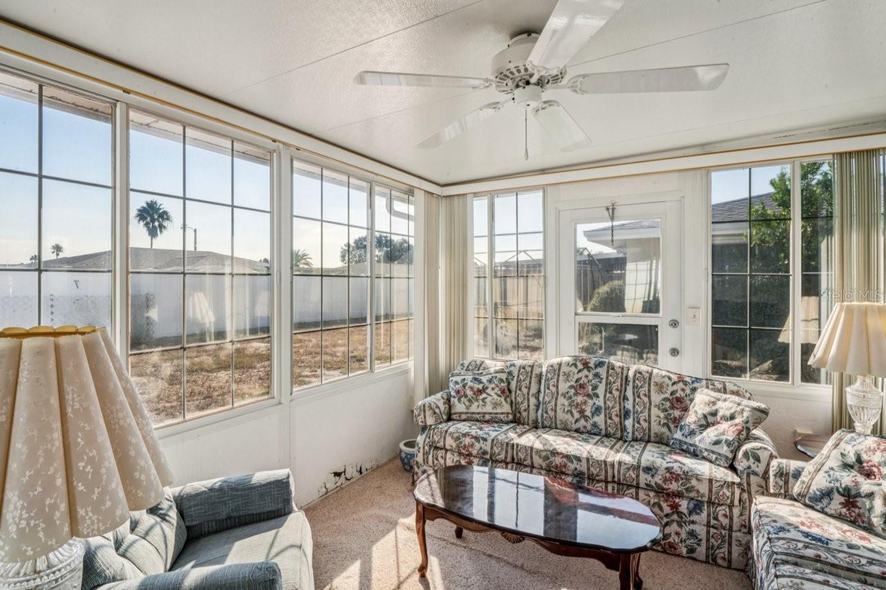 Sunroom has carpeting, lots of windows and ceiling fan.