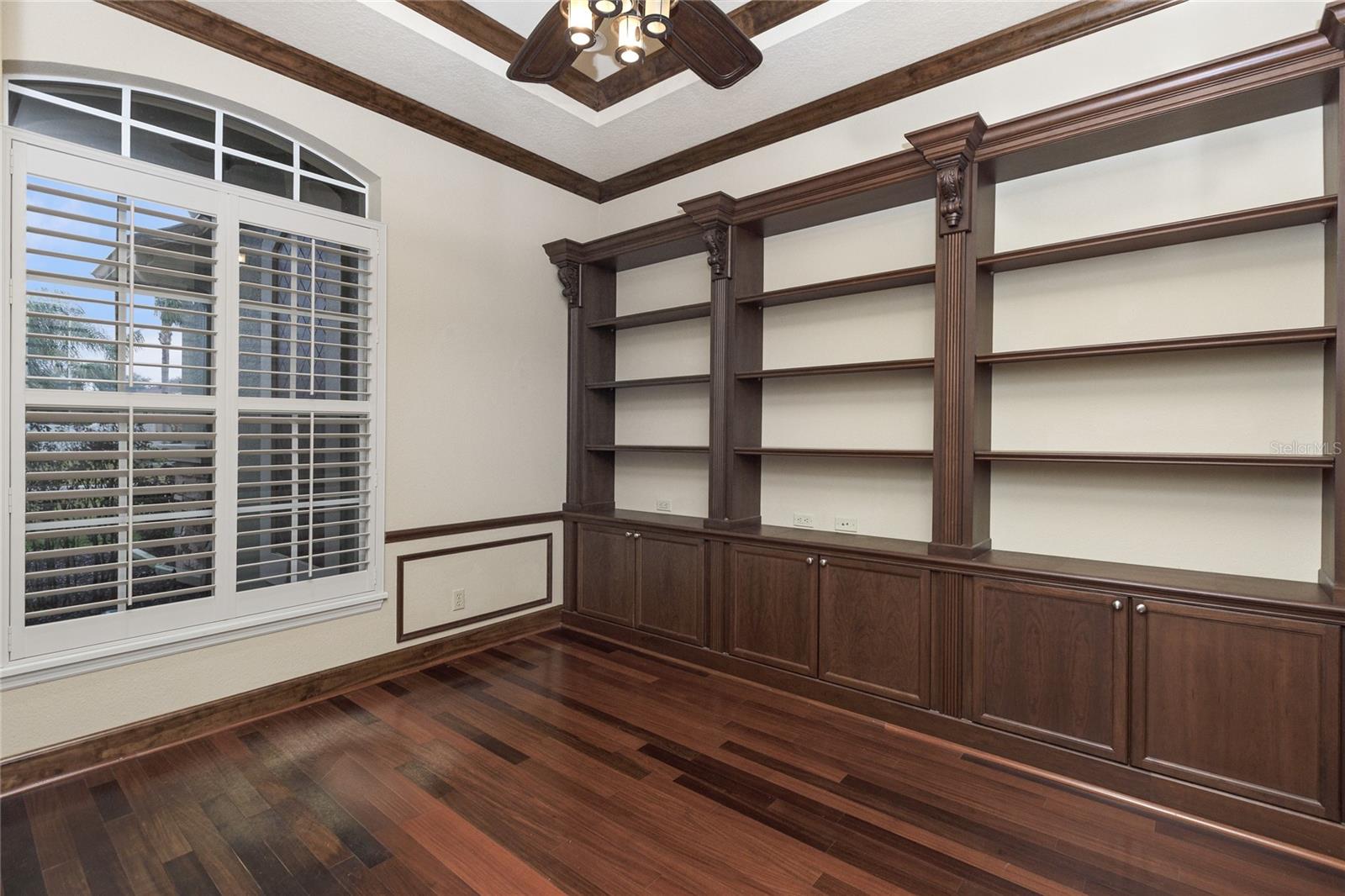 Office with built in bookshelves, wood flooring and plantation shutters