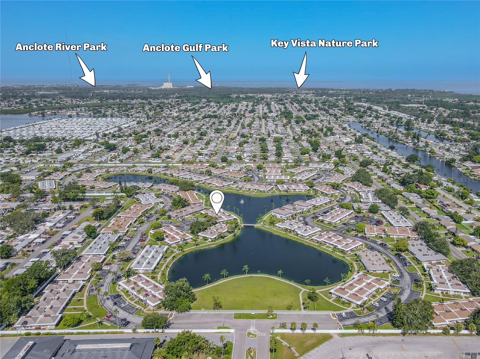 Aerial view of the beautifully maintained senior condo community showcasing landscaped grounds, walking paths, and surrounding green spaces. Nearby parks can be seen in the background, highlighting the community’s close proximity to outdoor recreation and peaceful natural surroundings.