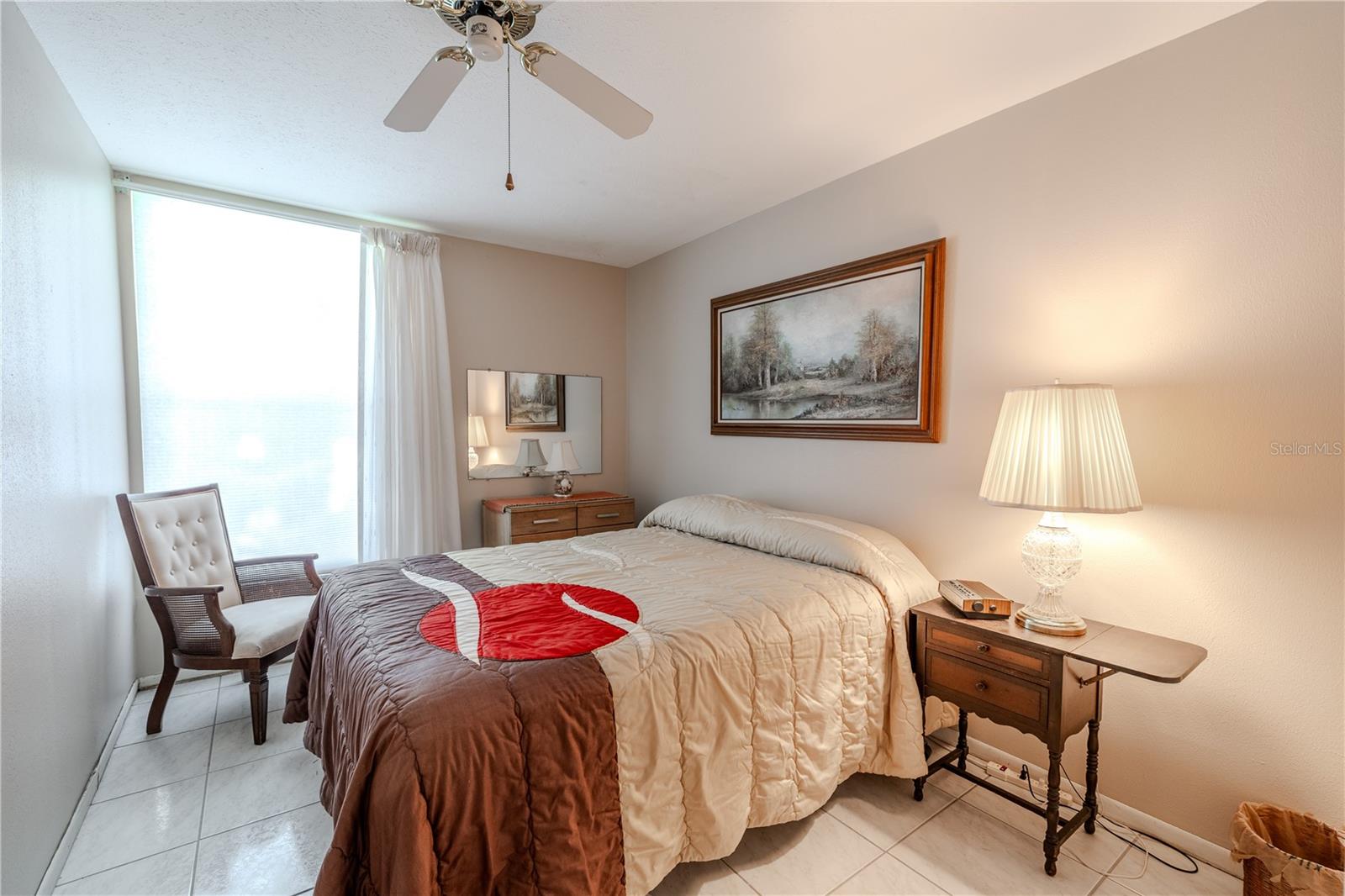 Bright and inviting second bedroom featuring a large window that bathes the room in natural sunlight, complemented by a ceiling fan for comfort. The built-in closet provides practical storage, while the airy, cheerful space is perfect for guests, a home office, or a personal retreat, offering versatility and a warm, welcoming atmosphere.