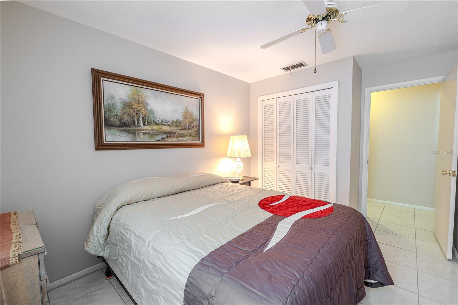 View of the second bedroom from the opposite side, highlighting the built-in closet and hallway entrance. Sunlight streams through the large window, creating a warm and inviting atmosphere. The room’s open, airy layout offers versatile space for guests, a home office, or a personal retreat, combining comfort, convenience, and a welcoming ambiance.