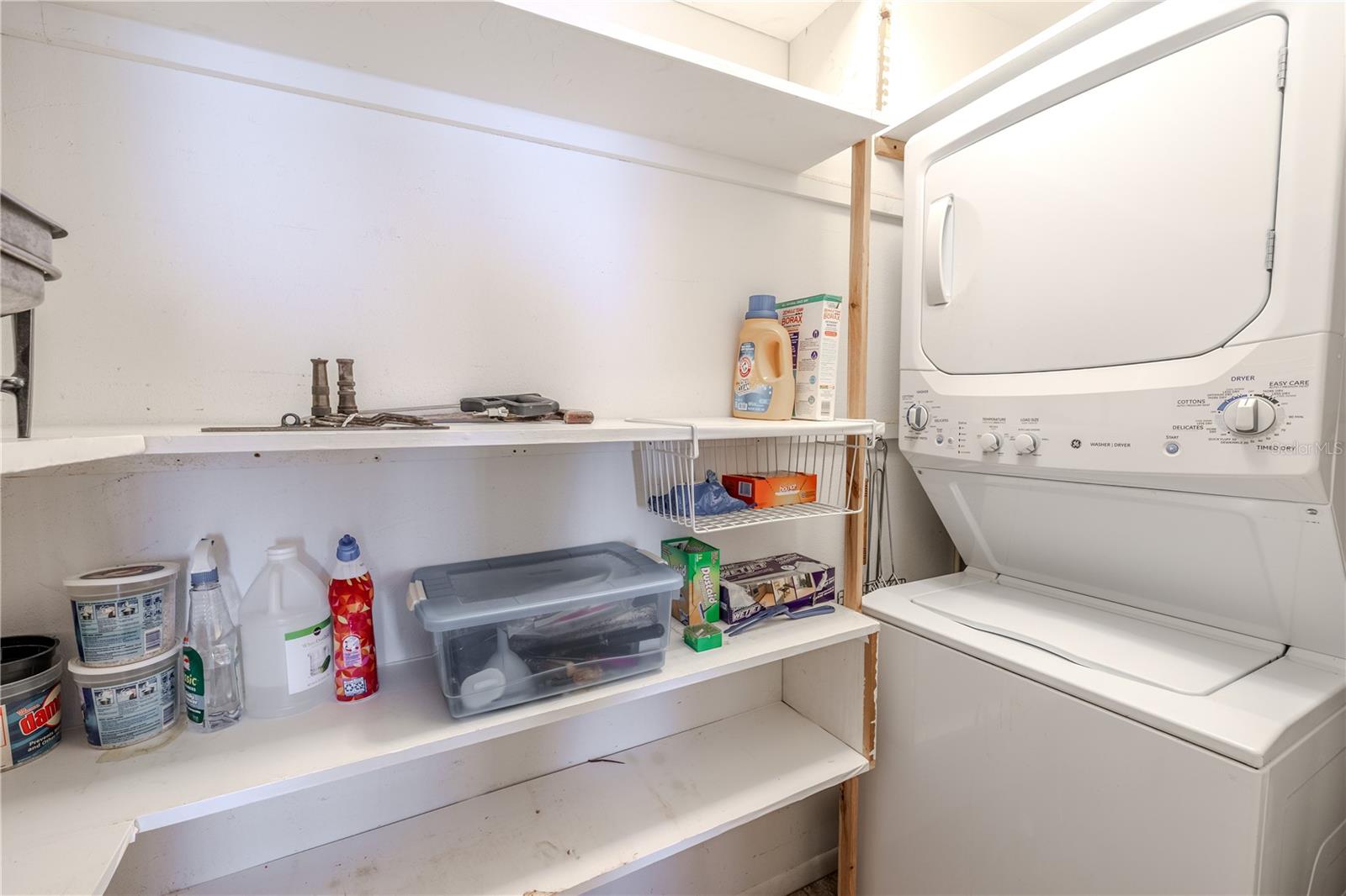 Full view of the primary bedroom’s walk-in closet with direct entry to the in-unit laundry—a true everyday convenience. The stacked washer/dryer and handy shelving keep chores easy and out of sight, so the bedroom stays calm and clutter-free.