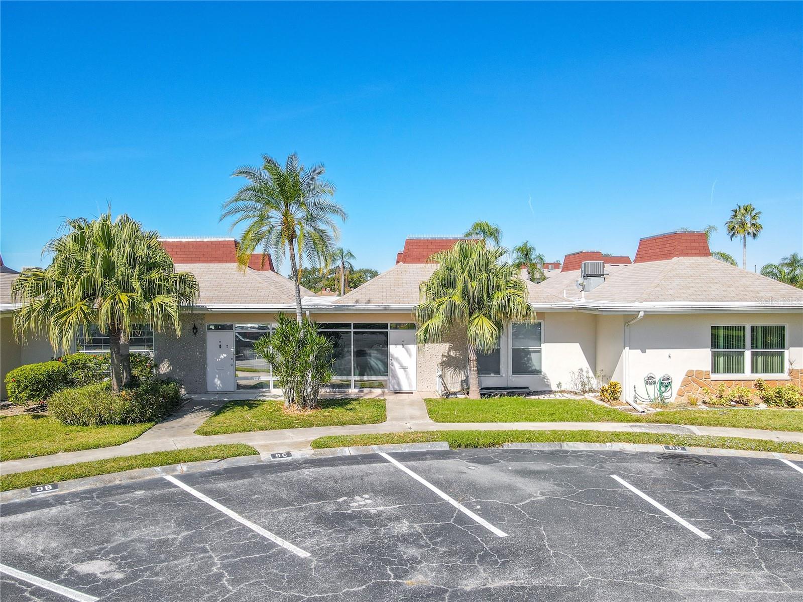 Ground-level view highlighting the assigned parking space conveniently located in front of the unit. Lush, well-maintained greenery surrounds the unit entrance, creating a serene and inviting setting while emphasizing both ease of access and the community’s beautifully landscaped environment.