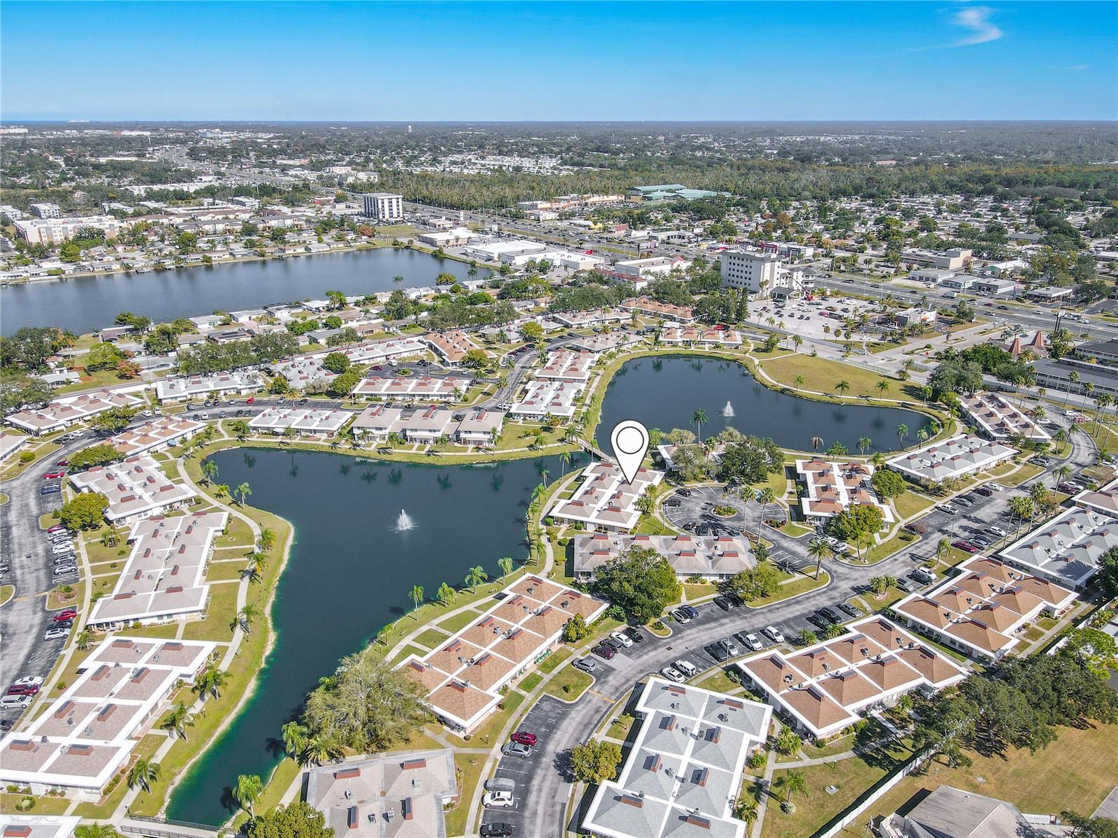 Aerial view of the beautifully maintained senior condo community showcasing landscaped grounds, highlighting close proximity of your unit to the palm tree lined walking path, crossing bridge and spacious parking.