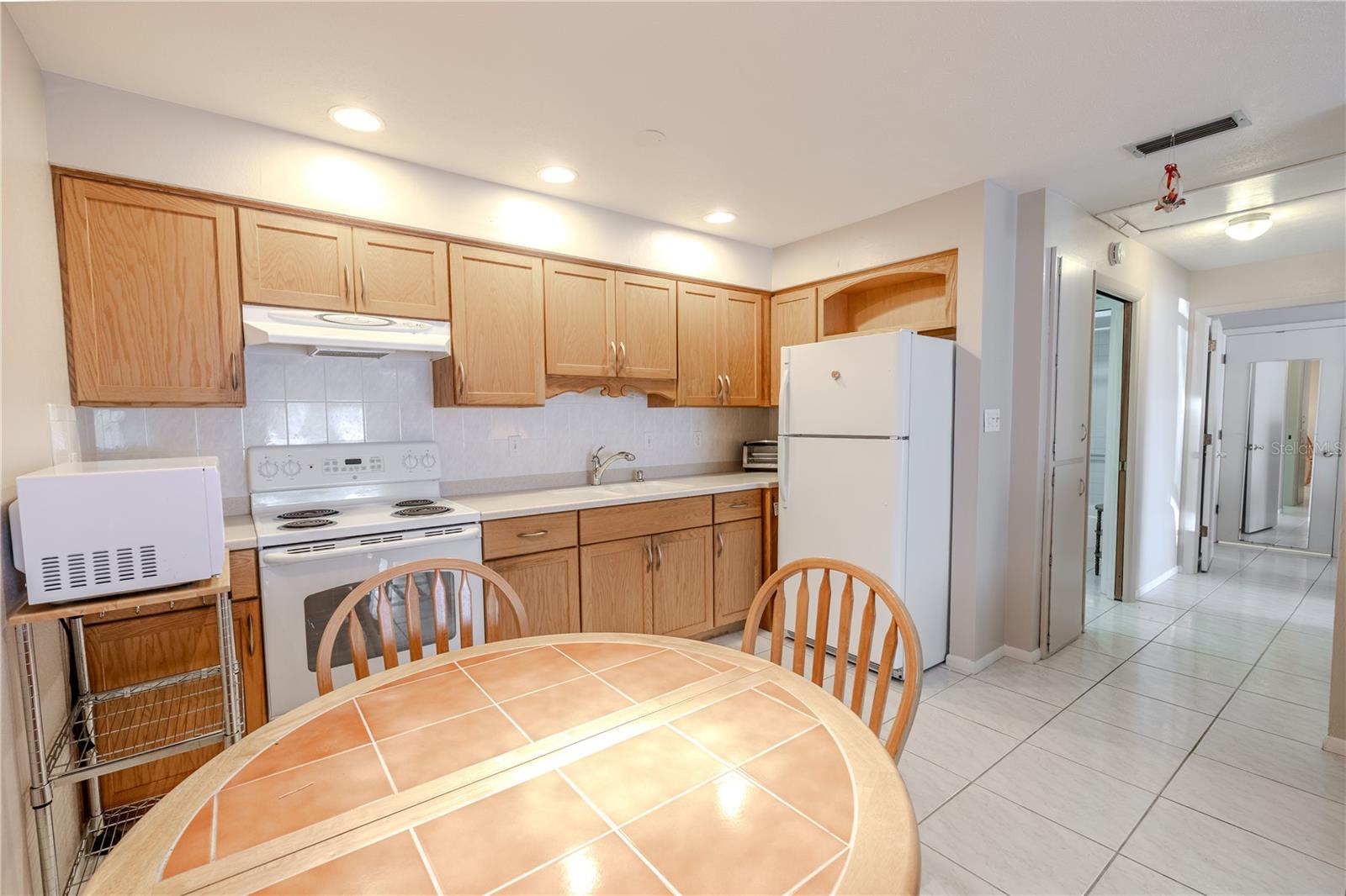 The kitchen’s full complement of appliances is showcased from the dining area, providing a functional and stylish backdrop for everyday cooking and entertaining. The combination of warm wood cabinets, durable Corian countertops, and appliances creates a welcoming and efficient space for both family meals and social gatherings.