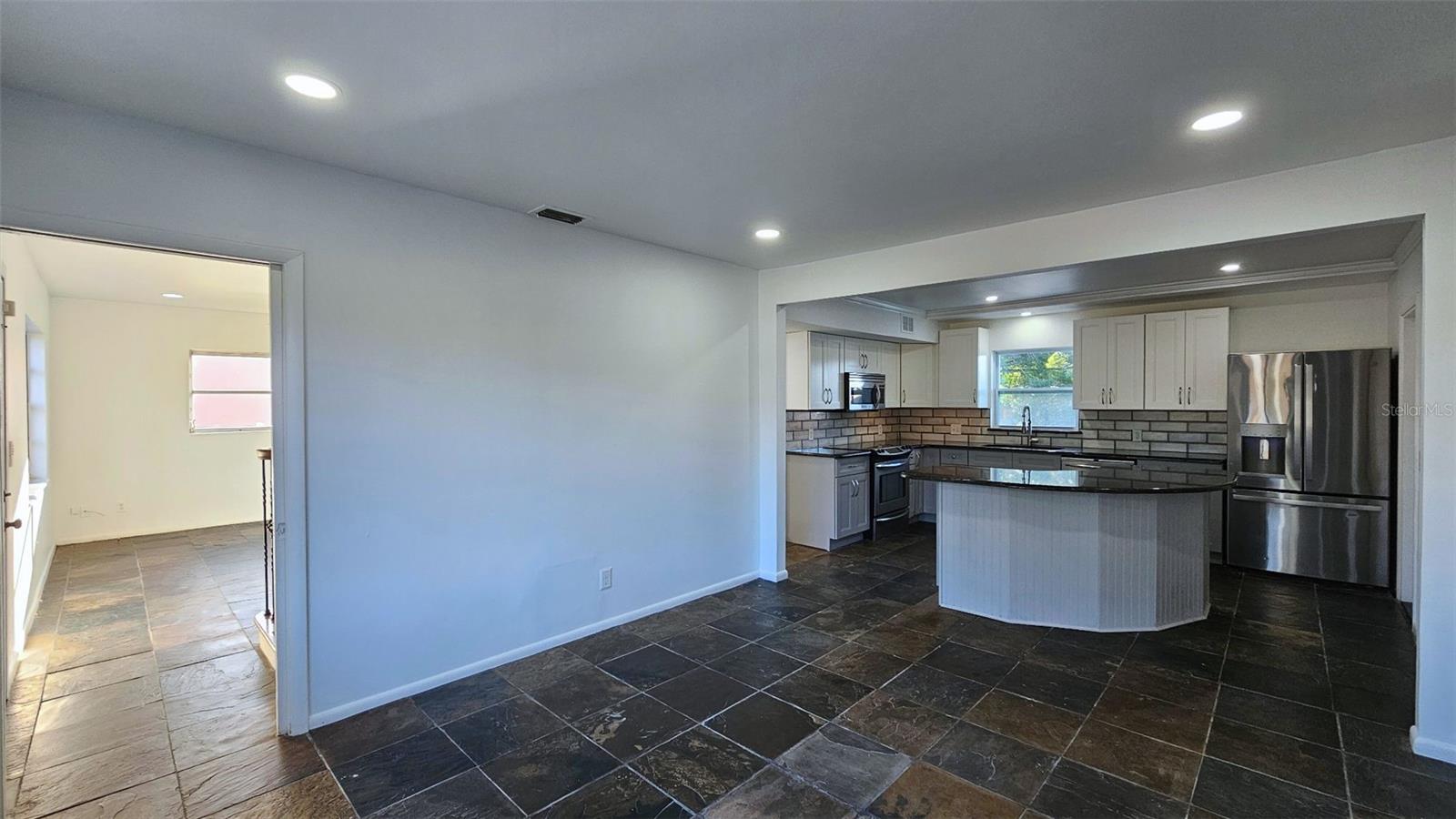 Dining area can accommodate very large dining table. Center island also offers bar stool seating. Natural morning light glowing in through living room background. cell phone photo.