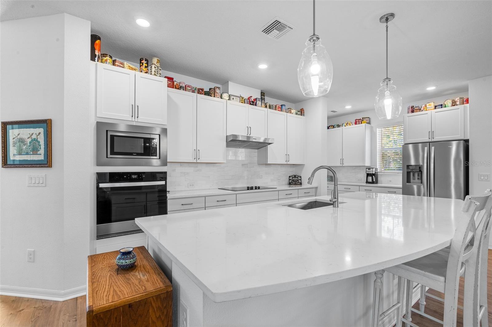 Bright white kitchen with stainless steel appliance package and a large island that functions as additional work space and casual eating space.