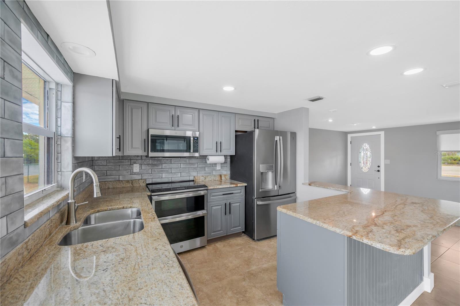 The updated kitchen features painted mahogany cabinets, granite countertops, upgraded stainless steel appliances, and stylish tile finishes.
